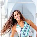 Eine lächelnde junge Frau mit langen, fliegenden braunen Haaren trägt ein farbenfrohes gestreiftes Neckholder-Top  lens: 56mm F1.4 DC DN | Contemporary 018