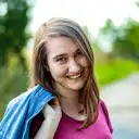 Lächelnde junge Frau mit Jeansjacke im Freien vor unscharfem grünen Hintergrund  lens: 56mm F1.4 DC DN | Contemporary 018