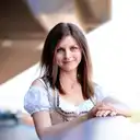 Eine lächelnde Frau im traditionellen Dirndl mit blauer Bluse und aufwendiger Stickerei blickt freundlich in die Kamera  lens: 56mm F1.4 DC DN | Contemporary 018