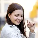 Eine lächelnde junge Frau mit dunklem Haar und hellem Strickpullover trägt einen herzförmigen Ohrring und blickt nach unten  lens: 56mm F1.4 DC DN | Contemporary 018