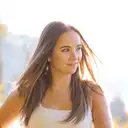 Porträt einer jungen Frau mit windzerzaustem, sonnenbeleuchtetem Haar und einem sanften Lächeln in einer hellen Außenumgebung  lens: 56mm F1.4 DC DN | Contemporary 018