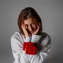 Porträt von Anja Stiftinger in einem weißen Hemd, deren Hände symbolisch durch einen breiten roten Lackgürtel gefesselt sind