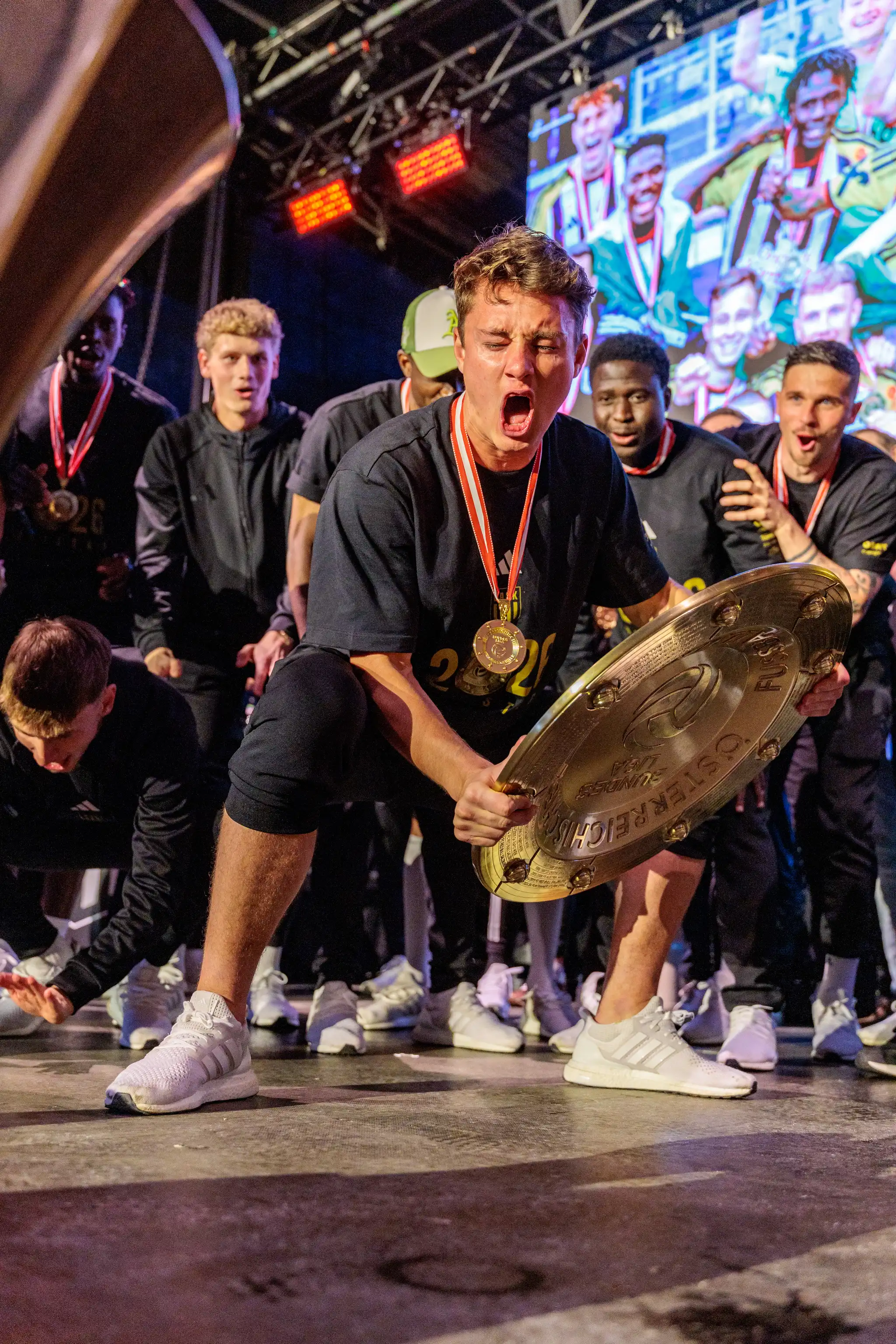 Ein LASK-Spieler hockt während der Meisterfeier in Linz und hält den Meisterteller voller Freude fest