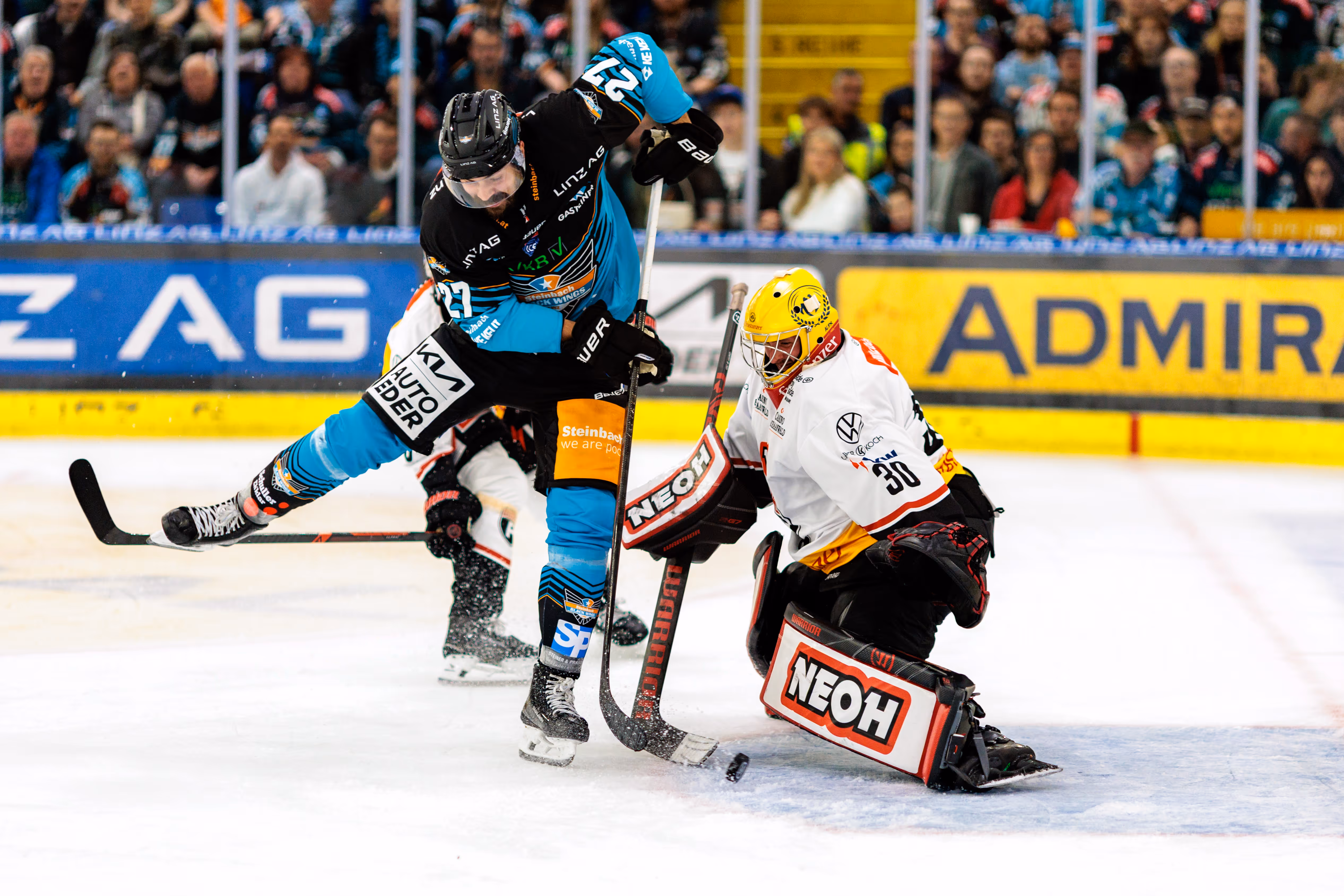 Eishockeyspieler Shawn St-Amant der Black Wings Linz schießt den Puck auf das Tor, während der Goalie der Pioneers Vorarlberg, Alex Caffi, versucht, diesen abzuwehren
