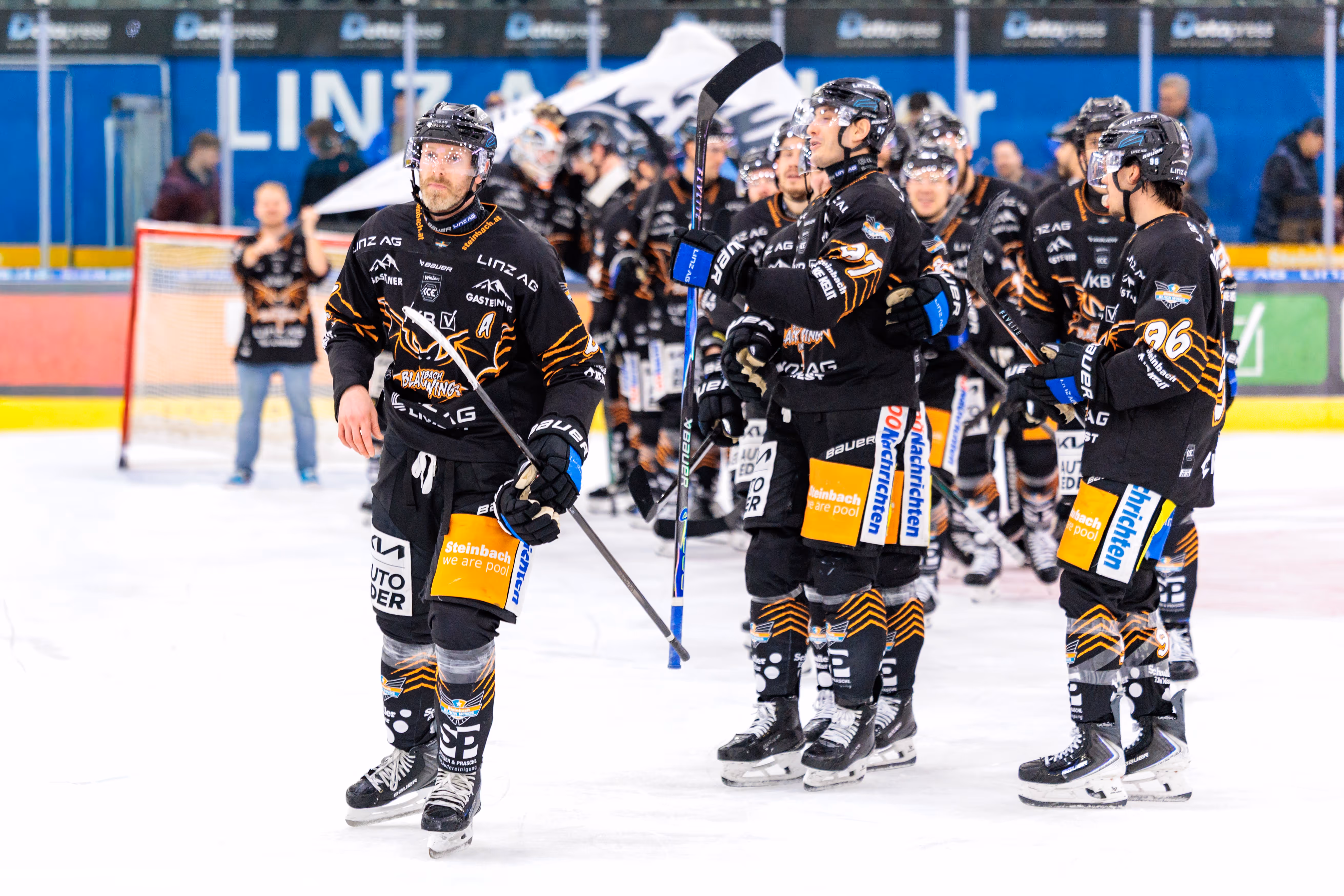 Der Eishockeyprofi Brian Lebler von den Black Wings Linz steht mit seinem Schläger auf dem Eis, umgeben von Teamkollegen in schwarzen Trikots