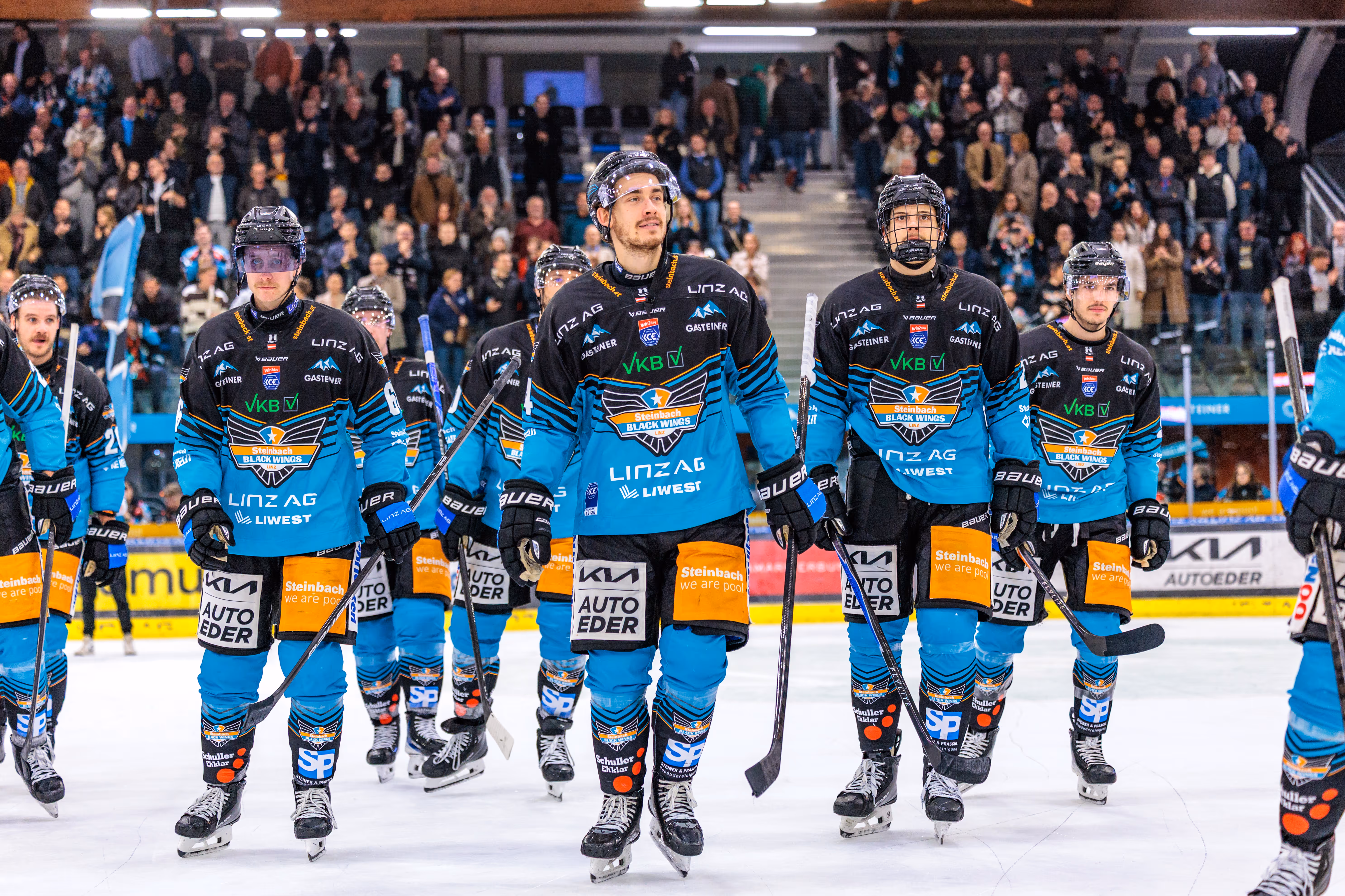 Die Eishockeymannschaft der Steinbach Black Wings Linz geht nach ihrem Sieg in einer Reihe bei der Ehrenrunde über das Eis, beobachtet von den Zuschauern auf der Tribüne