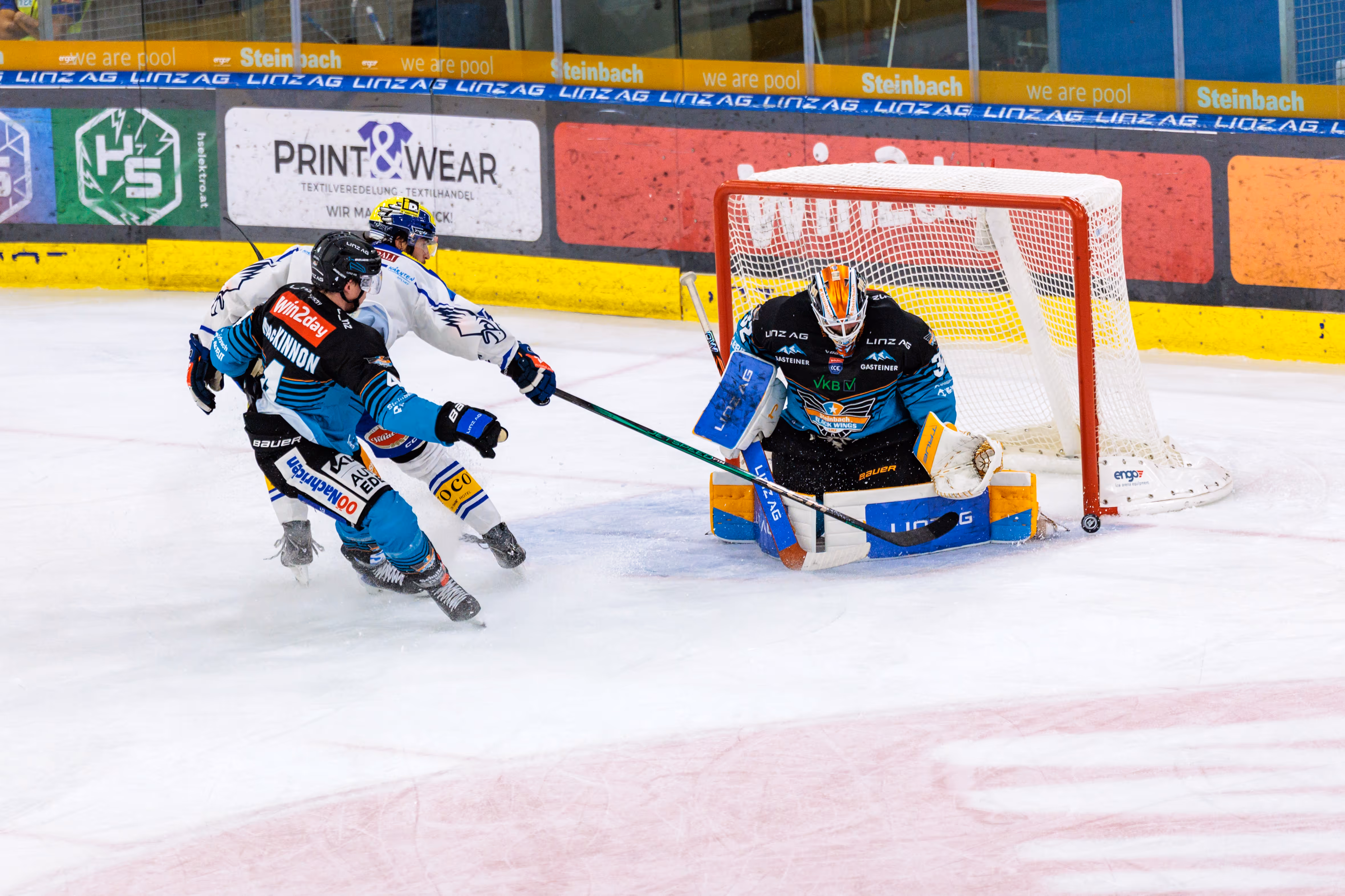 Eishockey-Torhüter Rasmus Tirronen von den Steinbach Black Wings Linz pariert einen Schuss, während Ryan MacKinnon und Adam Helewka vor dem Tor agieren