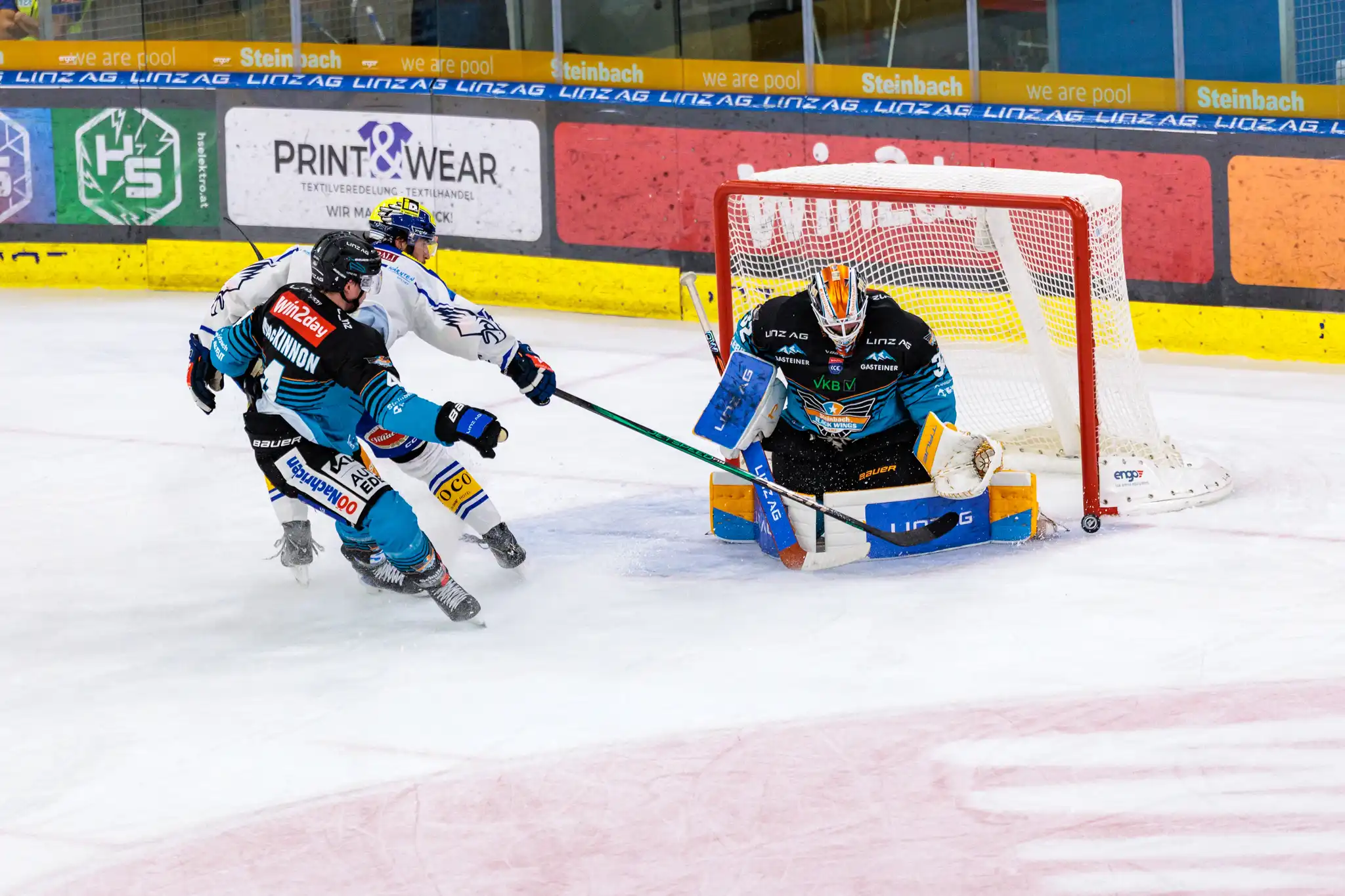 Eishockey-Torhüter Rasmus Tirronen von den Steinbach Black Wings Linz pariert einen Schuss, während Ryan MacKinnon und Adam Helewka vor dem Tor agieren
