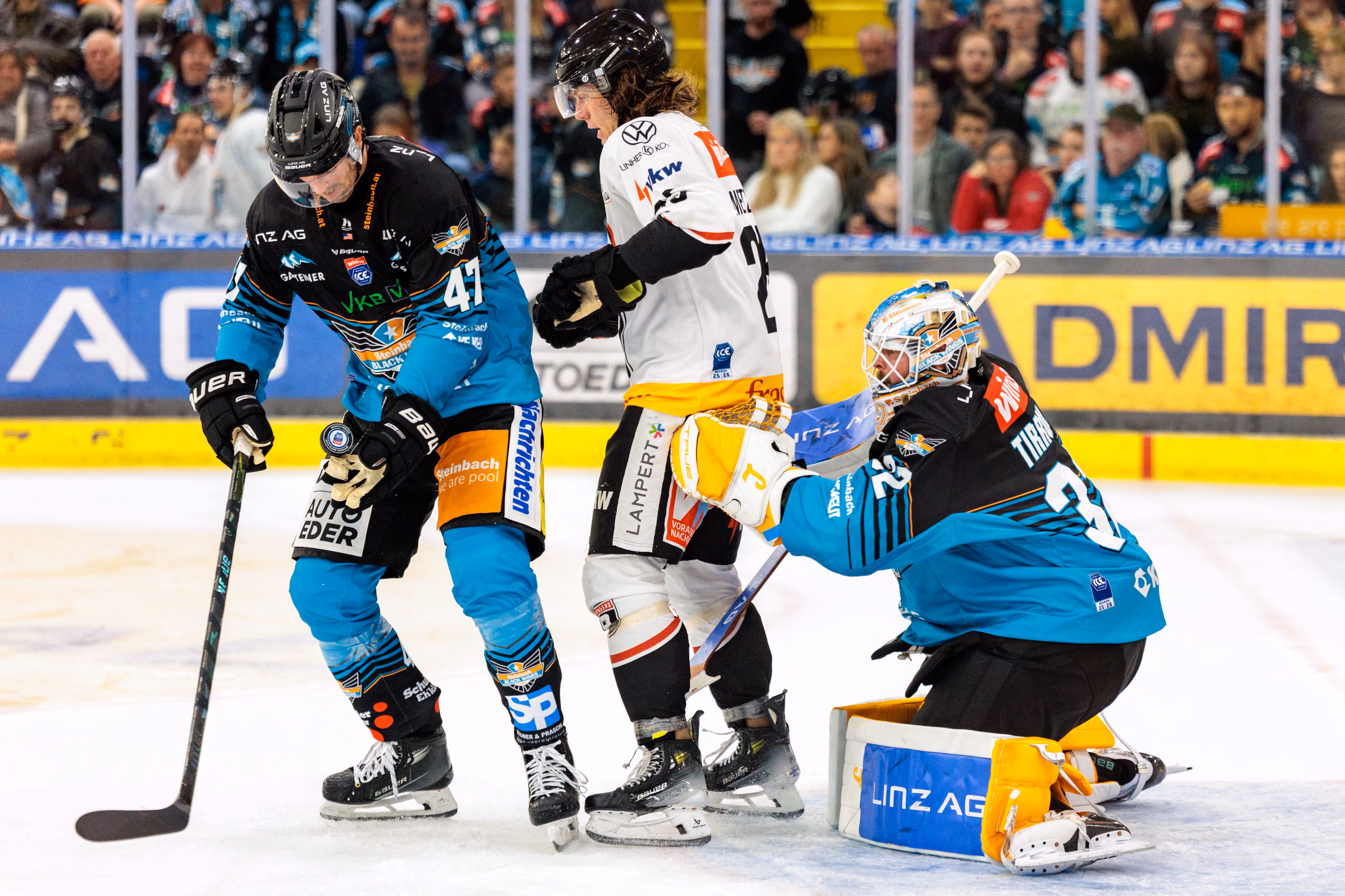 Eishockey-Torhüter Rasmus Tirronen von den Steinbach Black Wings Linz kniet zur Abwehr vor seinem Tor, während Julian Metzler und Logan Roe um den Puck kämpfen
