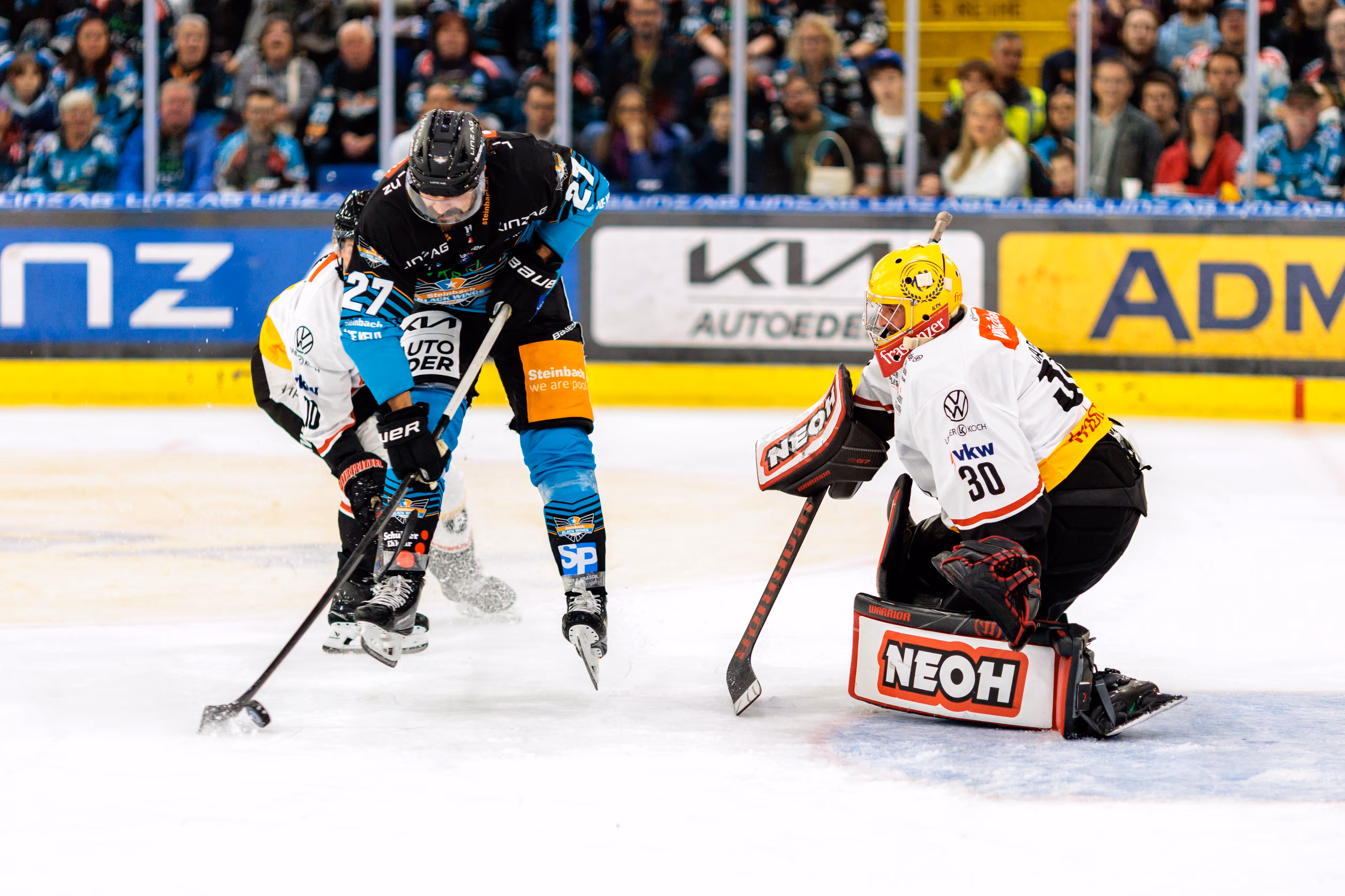 Eishockeyspieler Shawn St-Amant (Nr. 27) im schwarzen Trikot schießt den Puck auf das Tor, das von Goalie Alex Caffi (Nr. 30) im weißen Trikot verteidigt wird