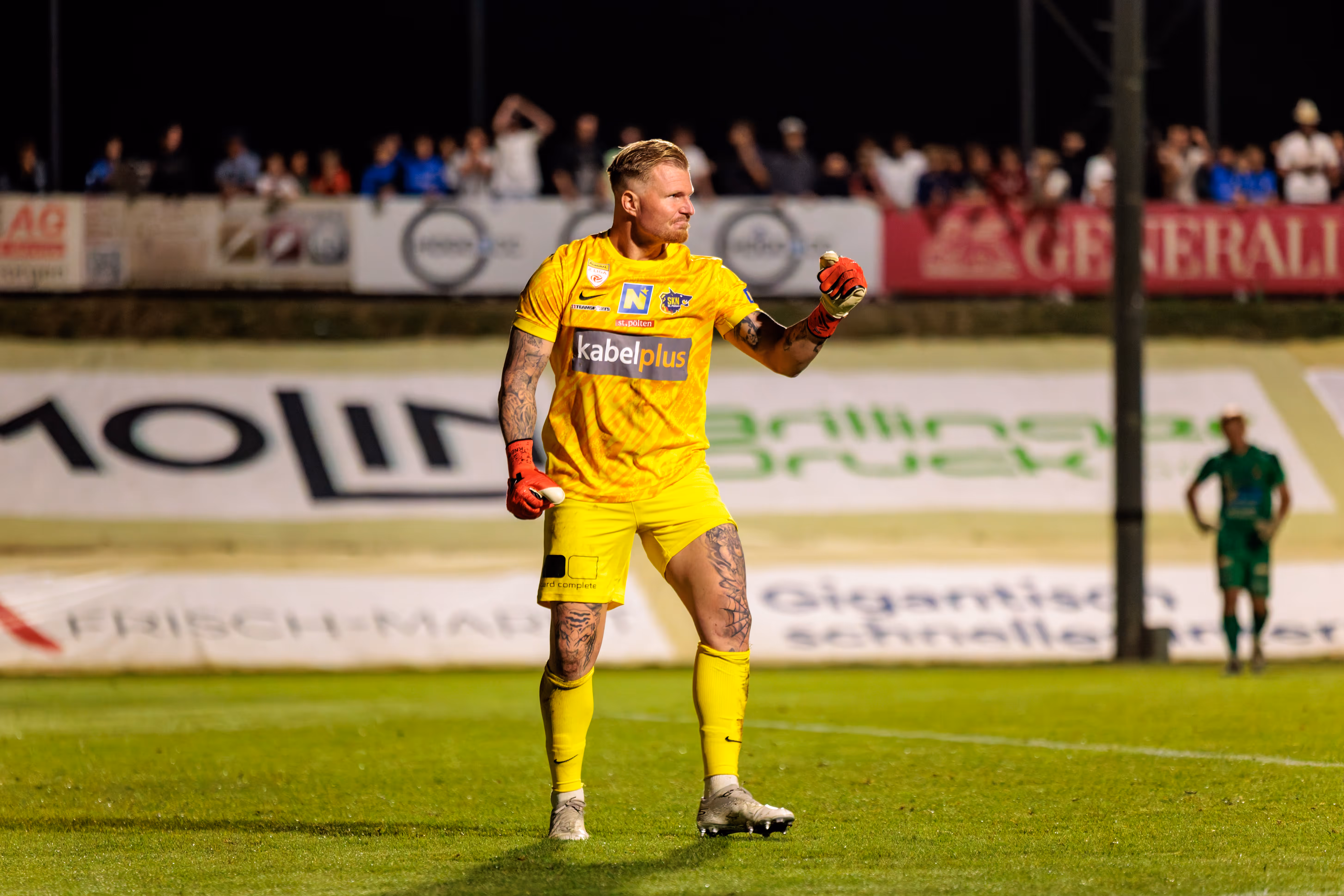 Der tätowierte Torwart von St. Pöten im gelben Trikot jubelt auf dem Feld bei einem ÖFB-Cup-Spiel unter Flutlicht