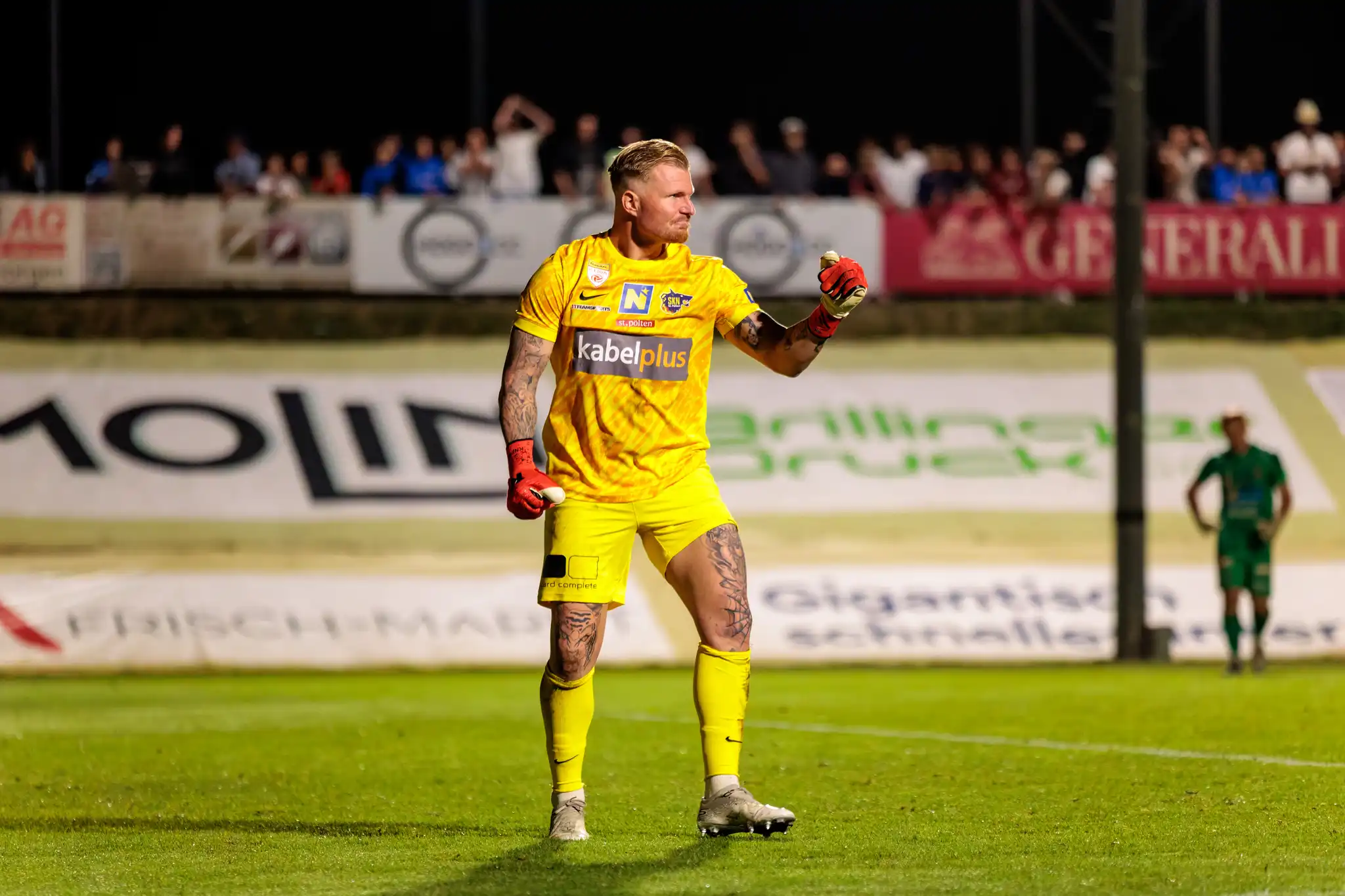 Der tätowierte Torwart von St. Pöten im gelben Trikot jubelt auf dem Feld bei einem ÖFB-Cup-Spiel unter Flutlicht