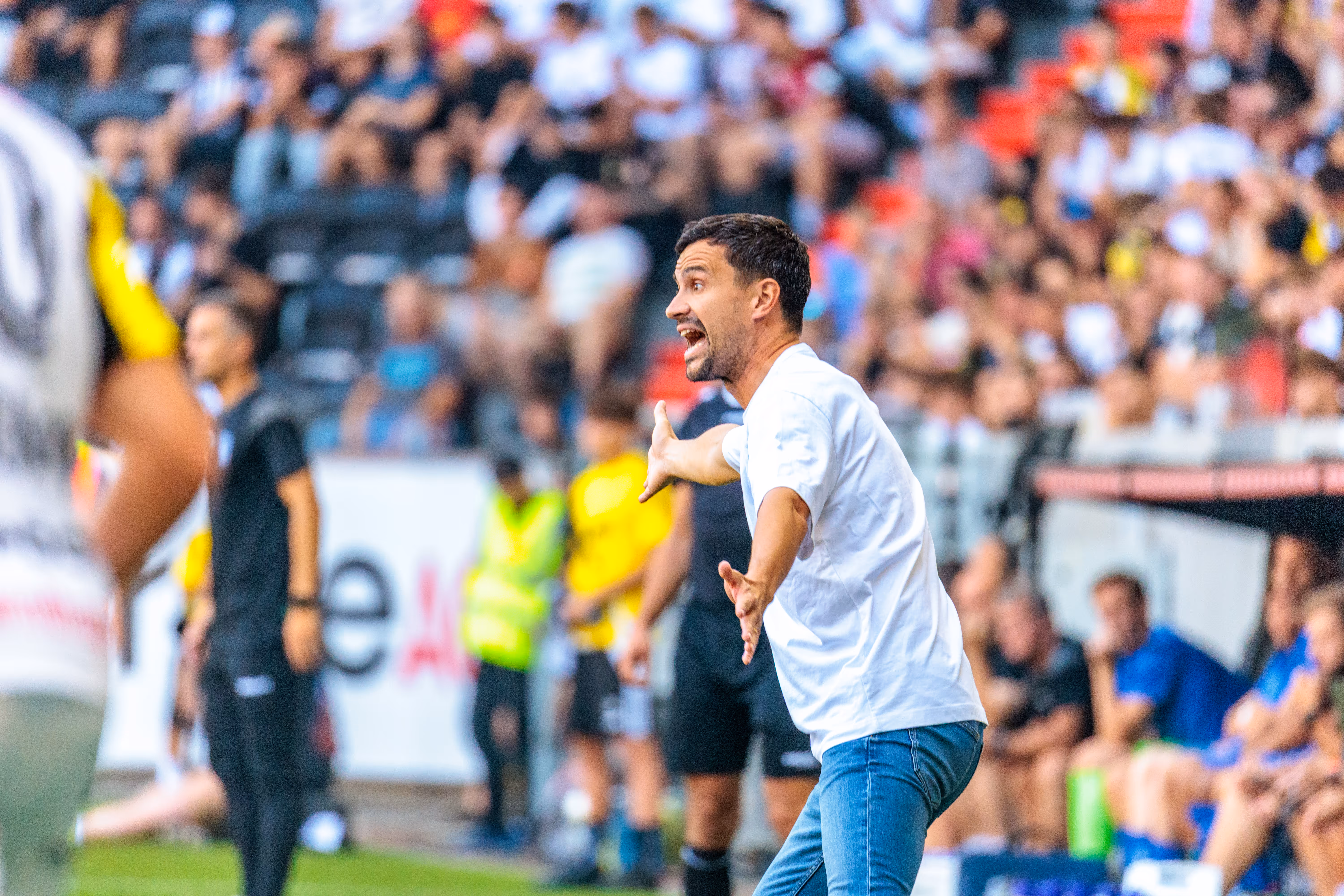 Der LASK-Trainer João Sacramento gibt am Spielfeldrand in einem weißen T-Shirt und Jeans mit energischer Geste und lautstarken Rufen Anweisungen an seine Mannschaft