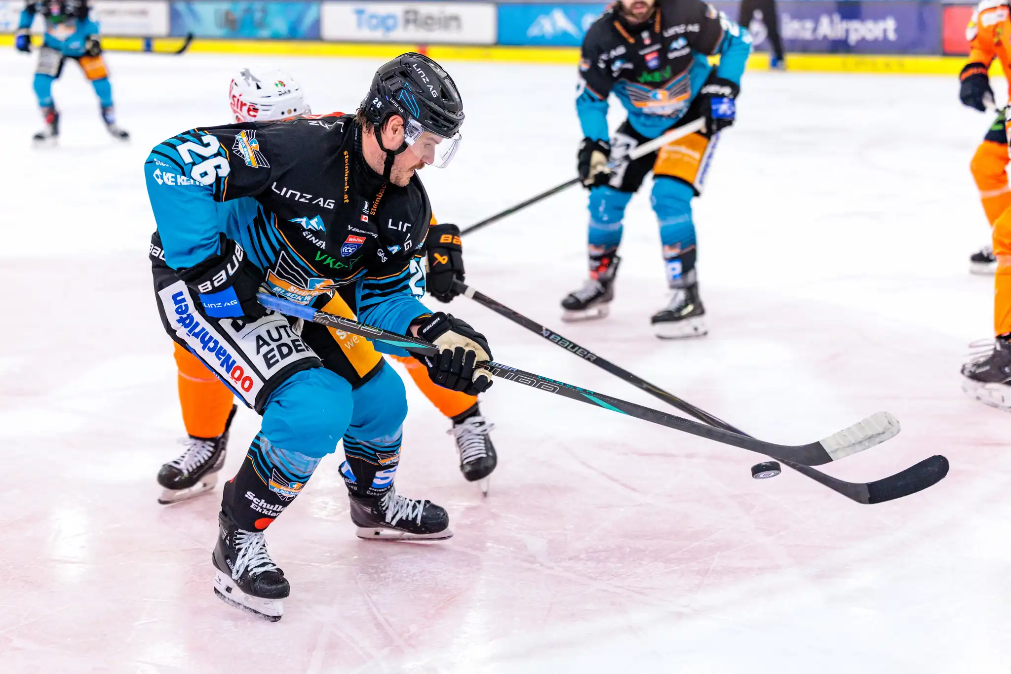Black Wings Linz Stürmer Travis Barron mit der Rückennummer 26 in einer dynamischen Szene während eines Eishockey-Spiels im Kampf um den Puck auf dem Eis