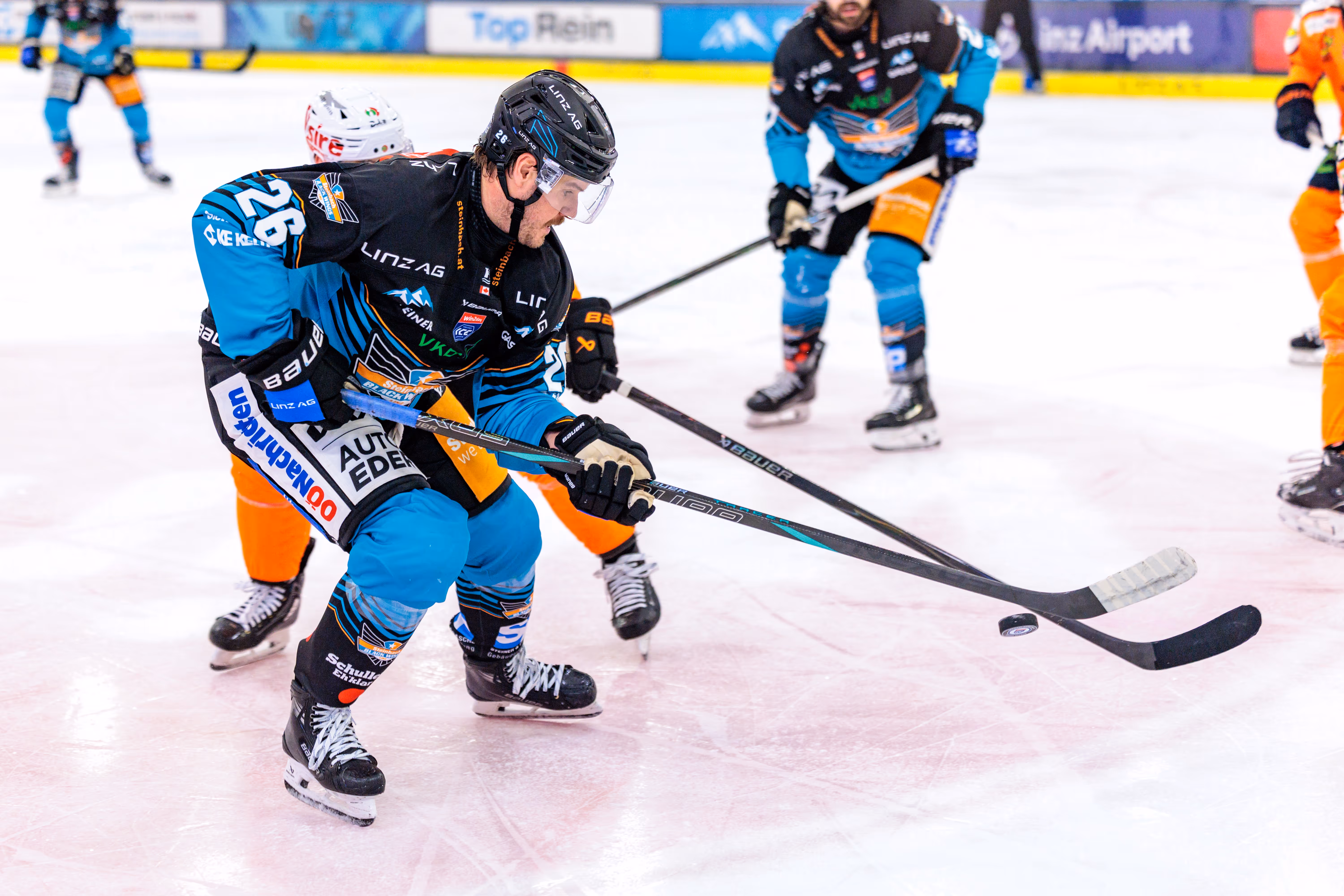 Black Wings Linz Stürmer Travis Barron mit der Rückennummer 26 in einer dynamischen Szene während eines Eishockey-Spiels im Kampf um den Puck auf dem Eis