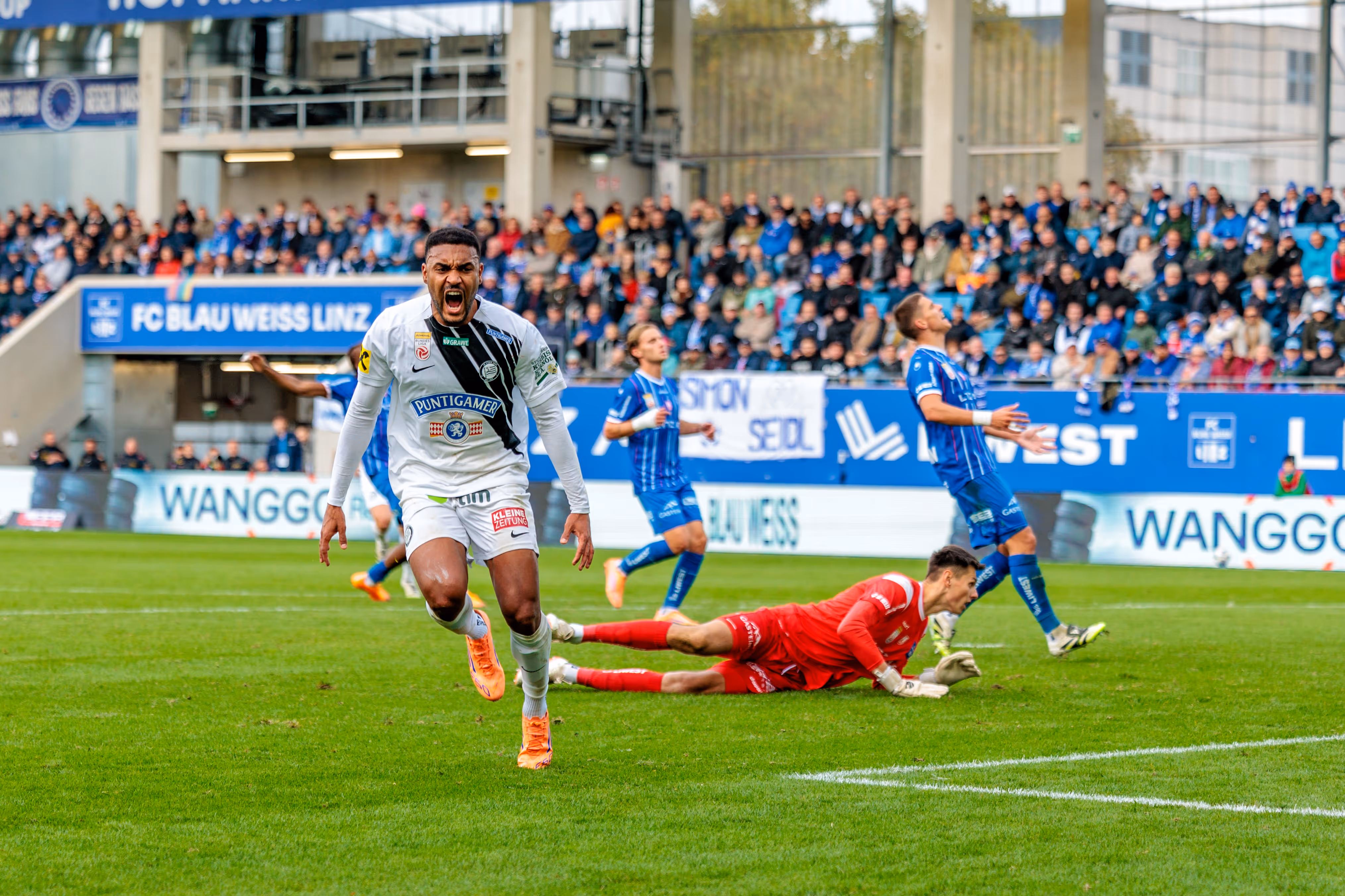 Sturm-Spieler Maurice Malone jubelt emotional über seinen Treffer gegen Blau-Weiß Linz, während der gegnerische Tormann geschlagen am Boden liegt