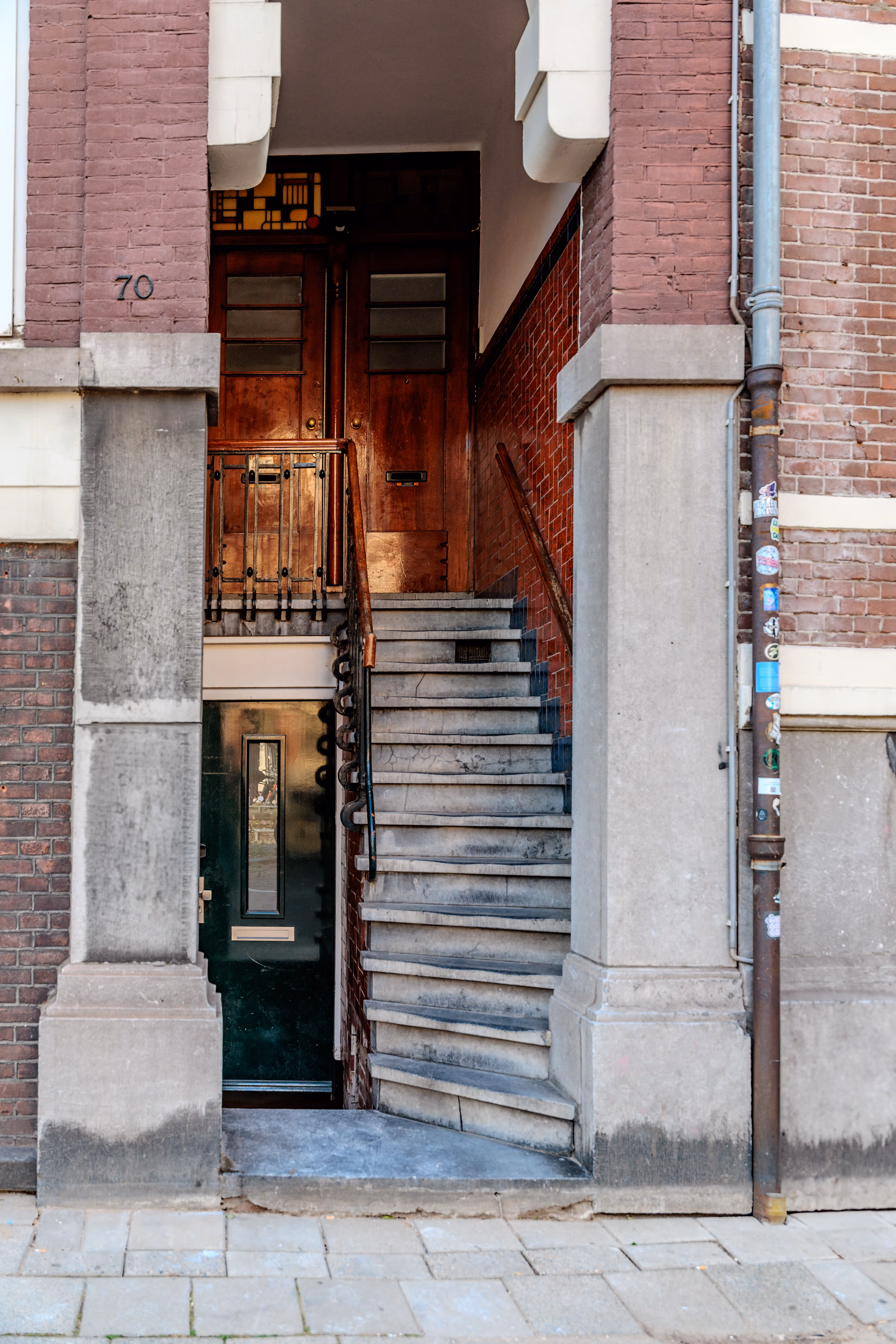 Die Hausnummer 70 kennzeichnet den charakteristischen Eingang eines Amsterdamer Backsteinhauses mit einer Steintreppe zur Holztür und einer weiteren Tür darunter 