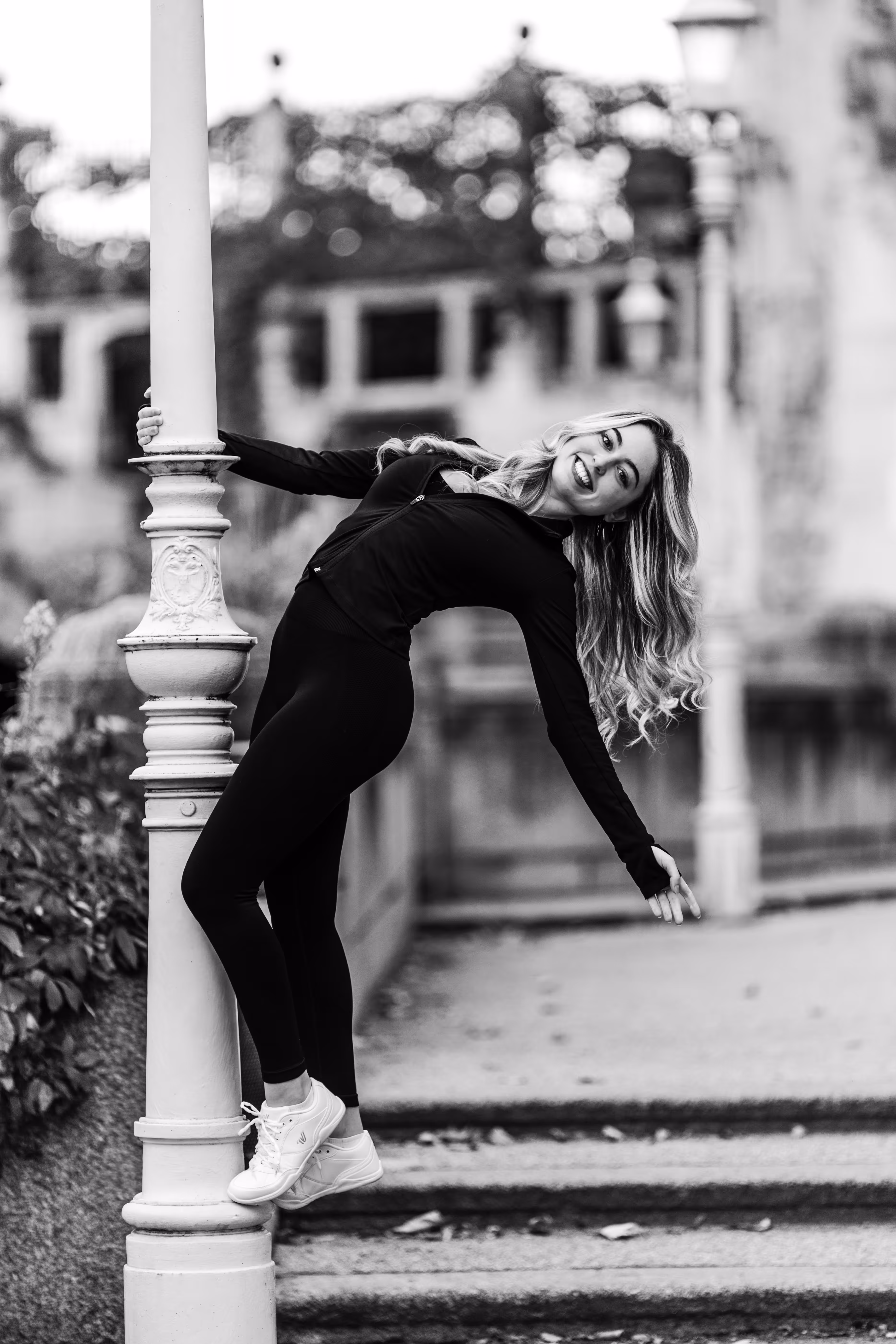 Schwarz-Weiß-Porträt von Model Valentina, die bei einem Fotoshooting im Wiener Stadtpark in sportlicher Kleidung lachend an einer Laterne posiert
