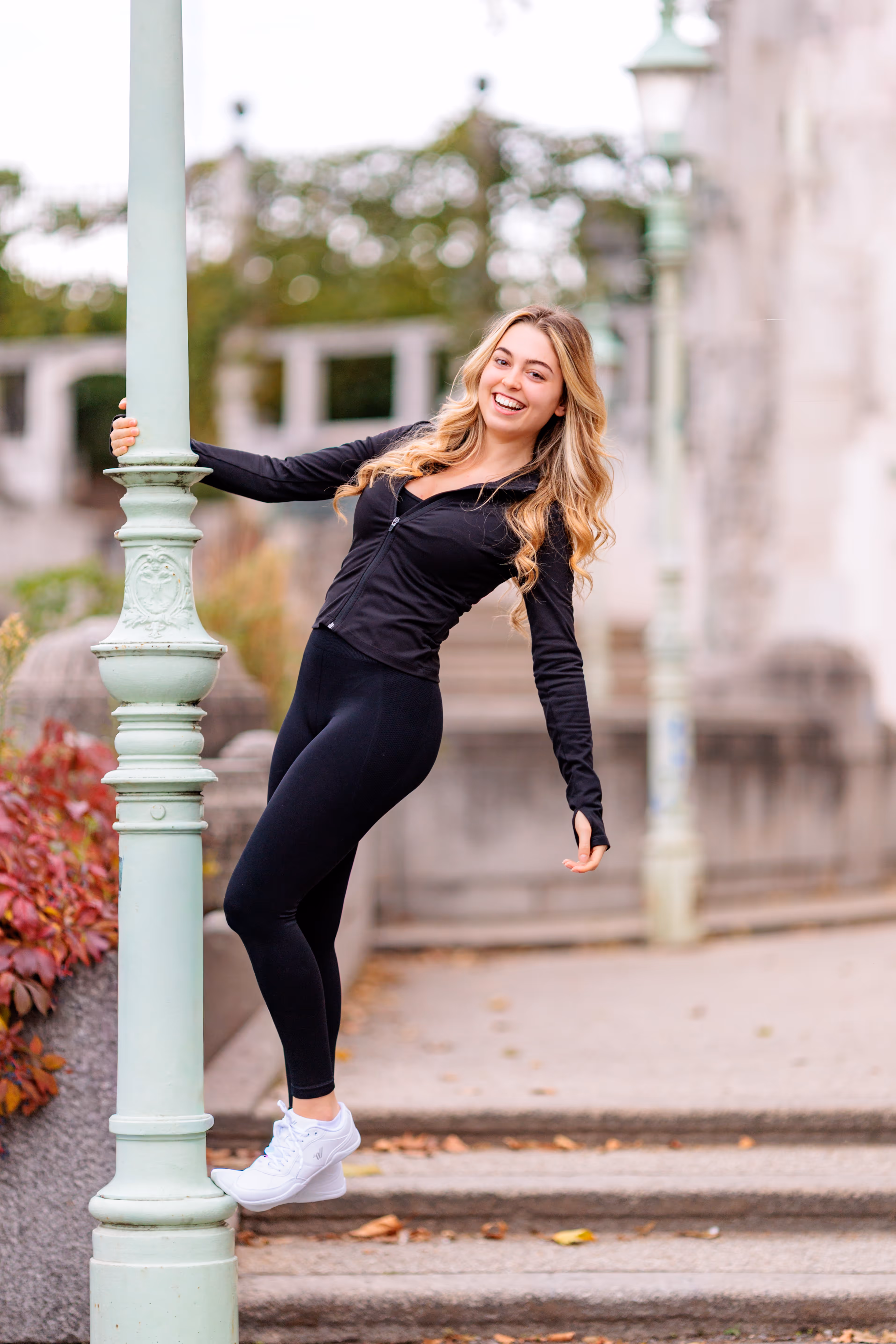 Model Valentina lehnt sich während ihres Fotoshootings im Wiener Stadtpark lachend und in schwarzer Sportkleidung an eine hellgrüne, verzierte Laterne