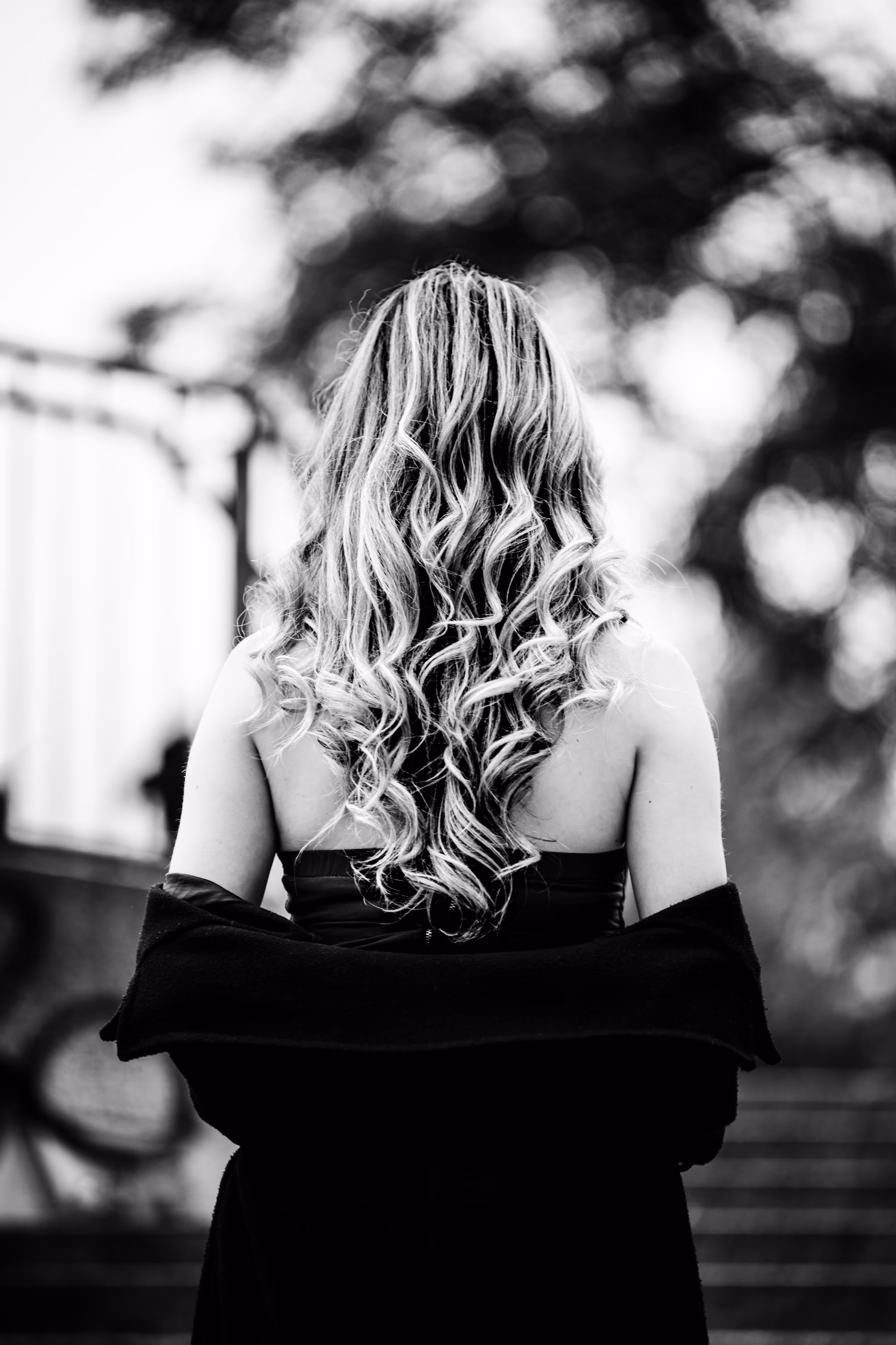 Schwarz-Weiß-Porträt von Model Valentina von hinten, deren lange, blonde Lockenpracht über ihre entblößten Schultern fällt