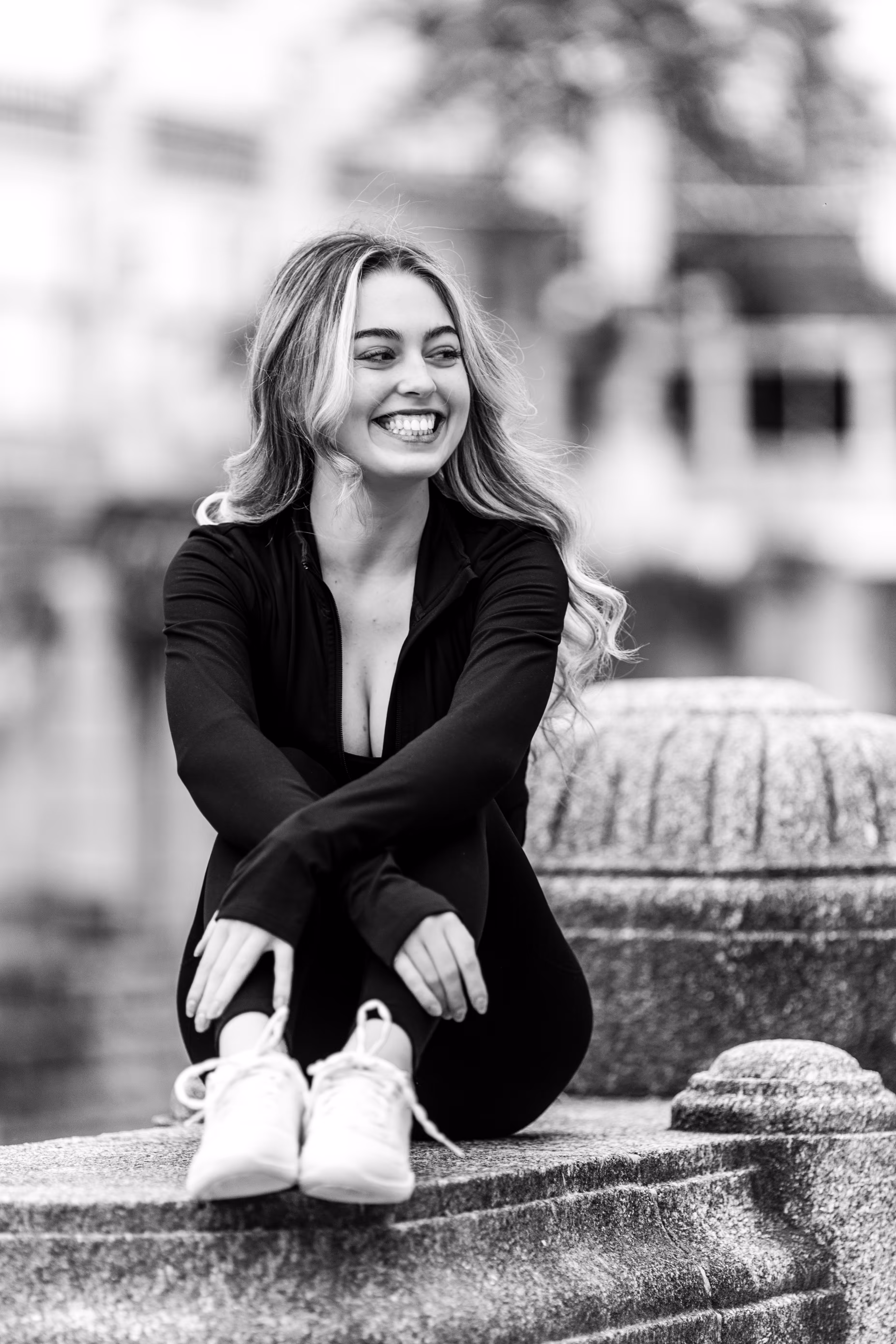 Schwarz-Weiß-Porträt von Model Valentina, die in sportlicher Kleidung lachend auf einer Steinbrüstung im Wiener Stadtpark sitzt
