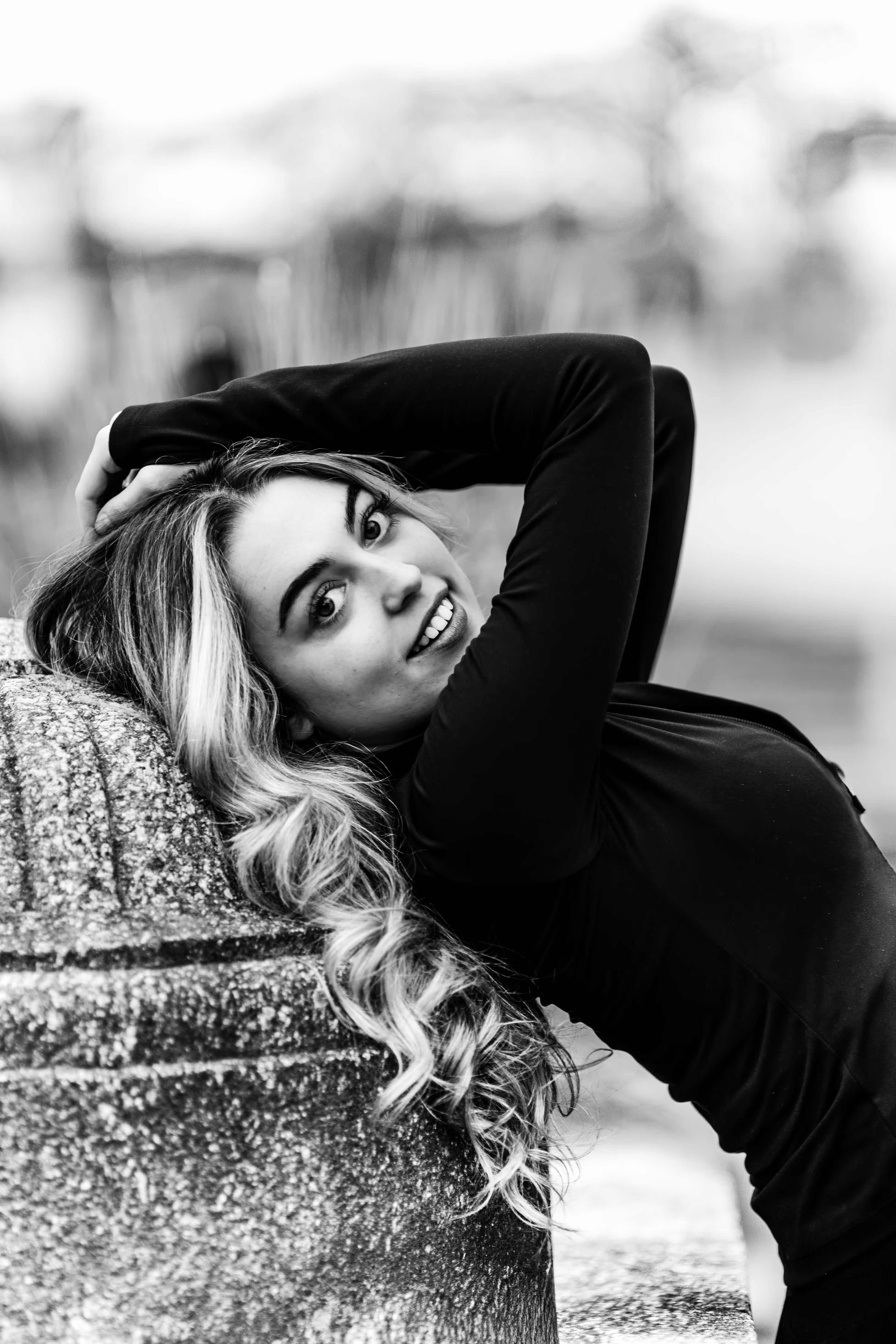 Schwarz-Weiß-Porträt von Model Valentina, die sich im Wiener Stadtpark an einen Stein lehnt, ihre Hände hinter dem Kopf verschränkt hat und direkt in die Kamera blickt