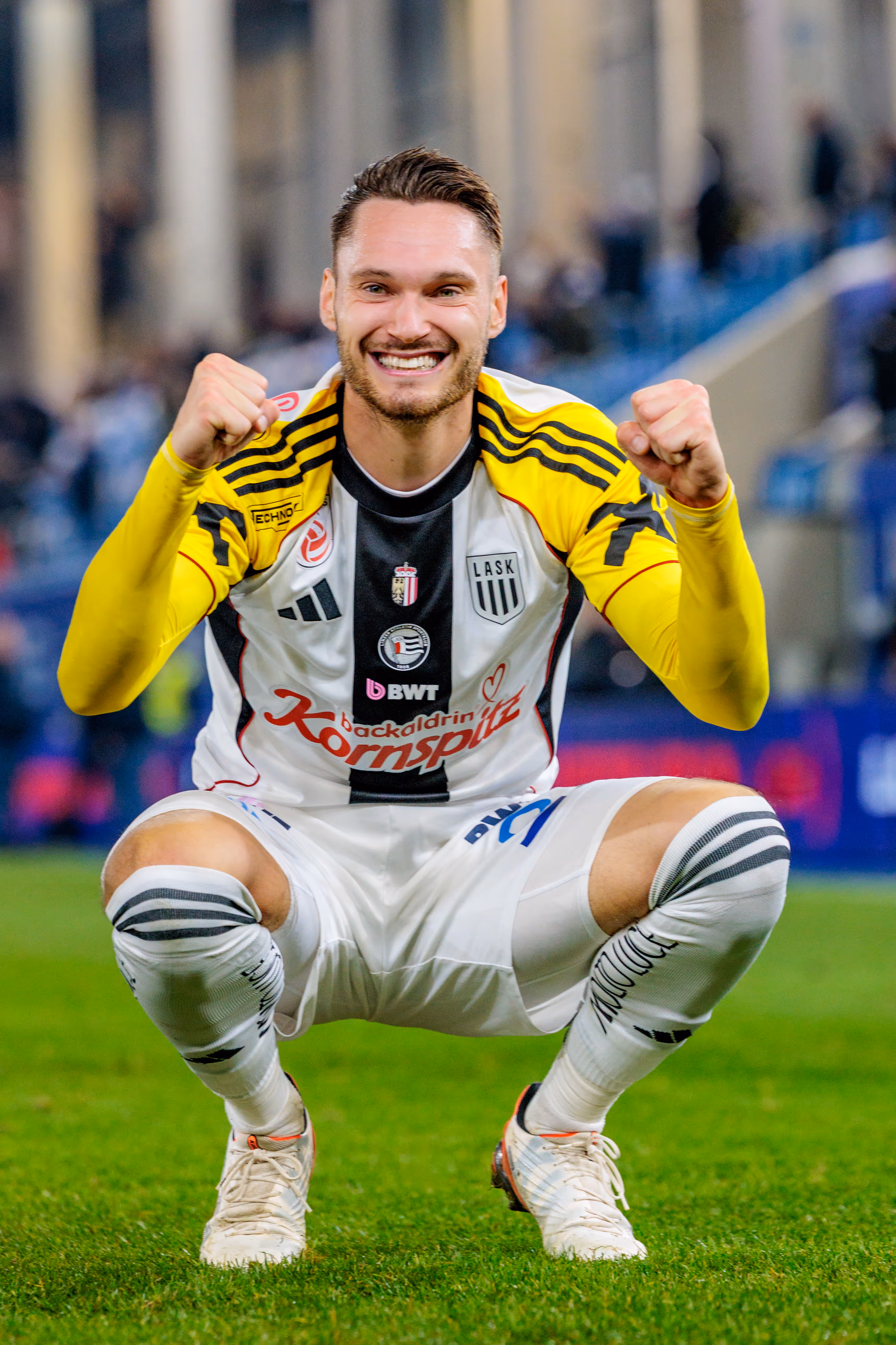 Der LASK-Spieler Valon Berisha geht in die Hocke, lächelt breit in die Kamera und ballt jubelnd seine Fäuste nach dem Spiel
