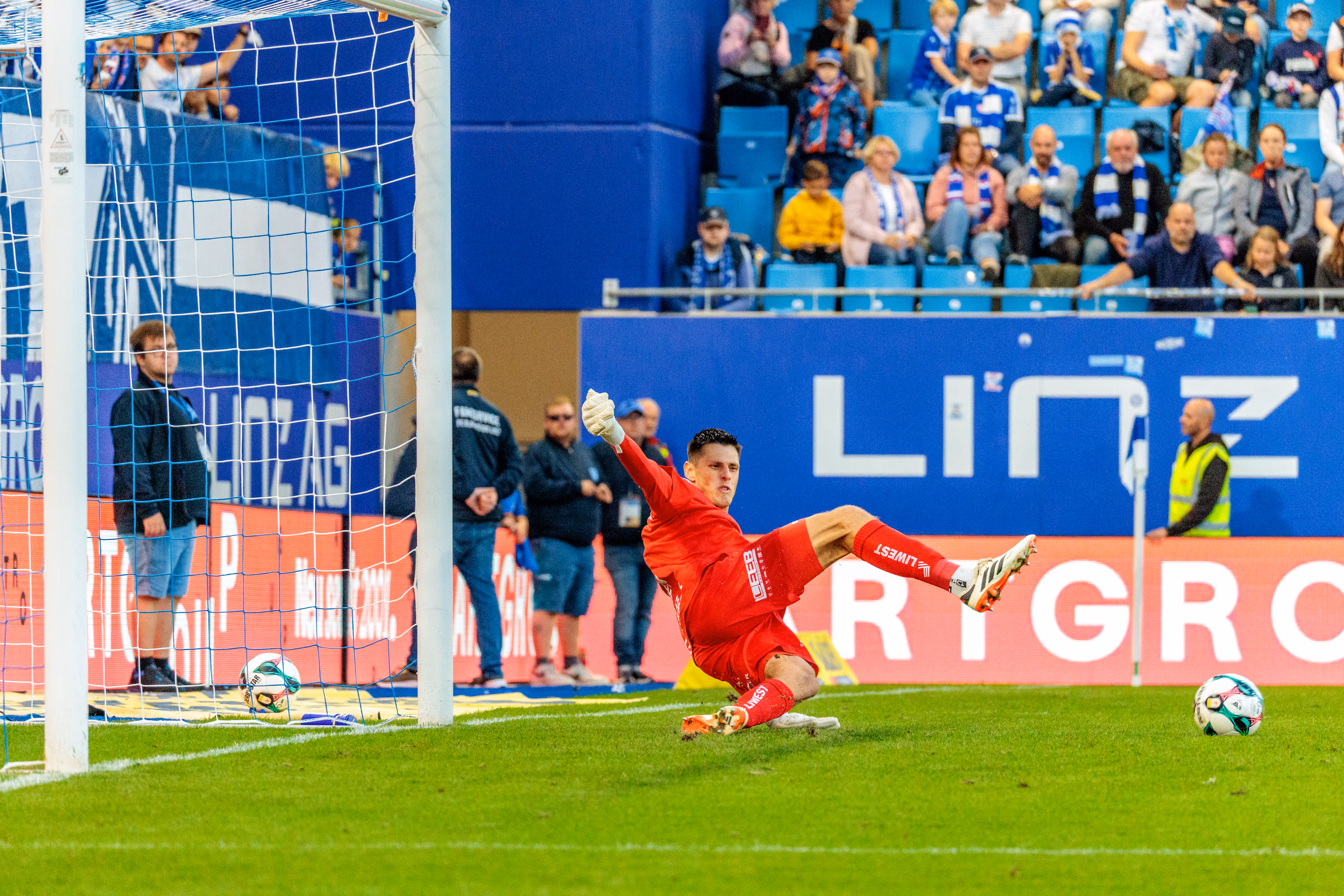 Der Torhüter von Blau-Weiß Linz, Viktor Baier, in seinem leuchtend roten Trikot bei einer spektakulären Parade während des Bundesligaspiels gegen Altach
