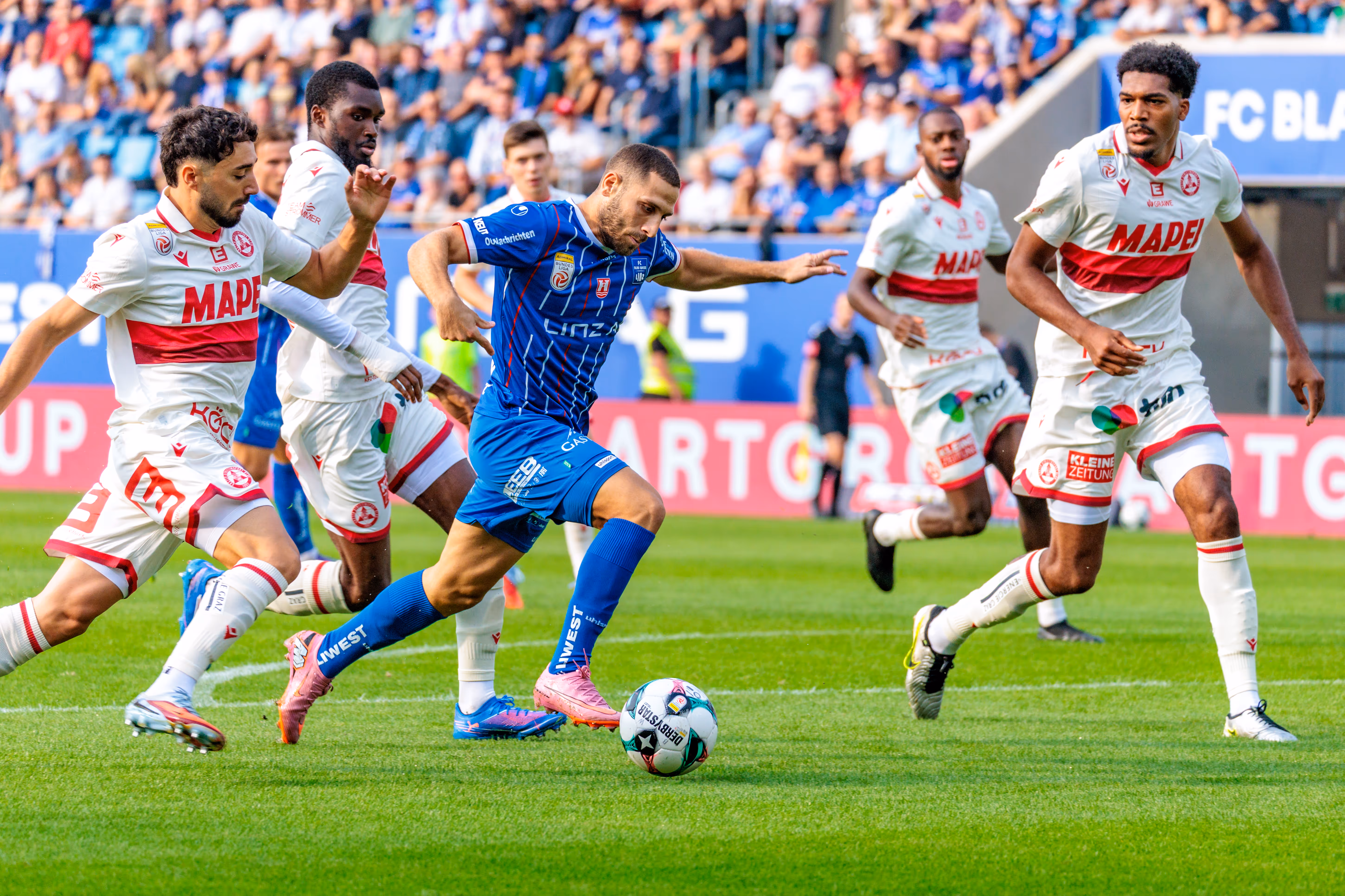 Der Stürmer von Blau-Weiß Linz, Shon Weissman, dribbelt im Bundesliga-Spiel dynamisch am Ball, bedrängt von mehreren Verteidigern des GAK