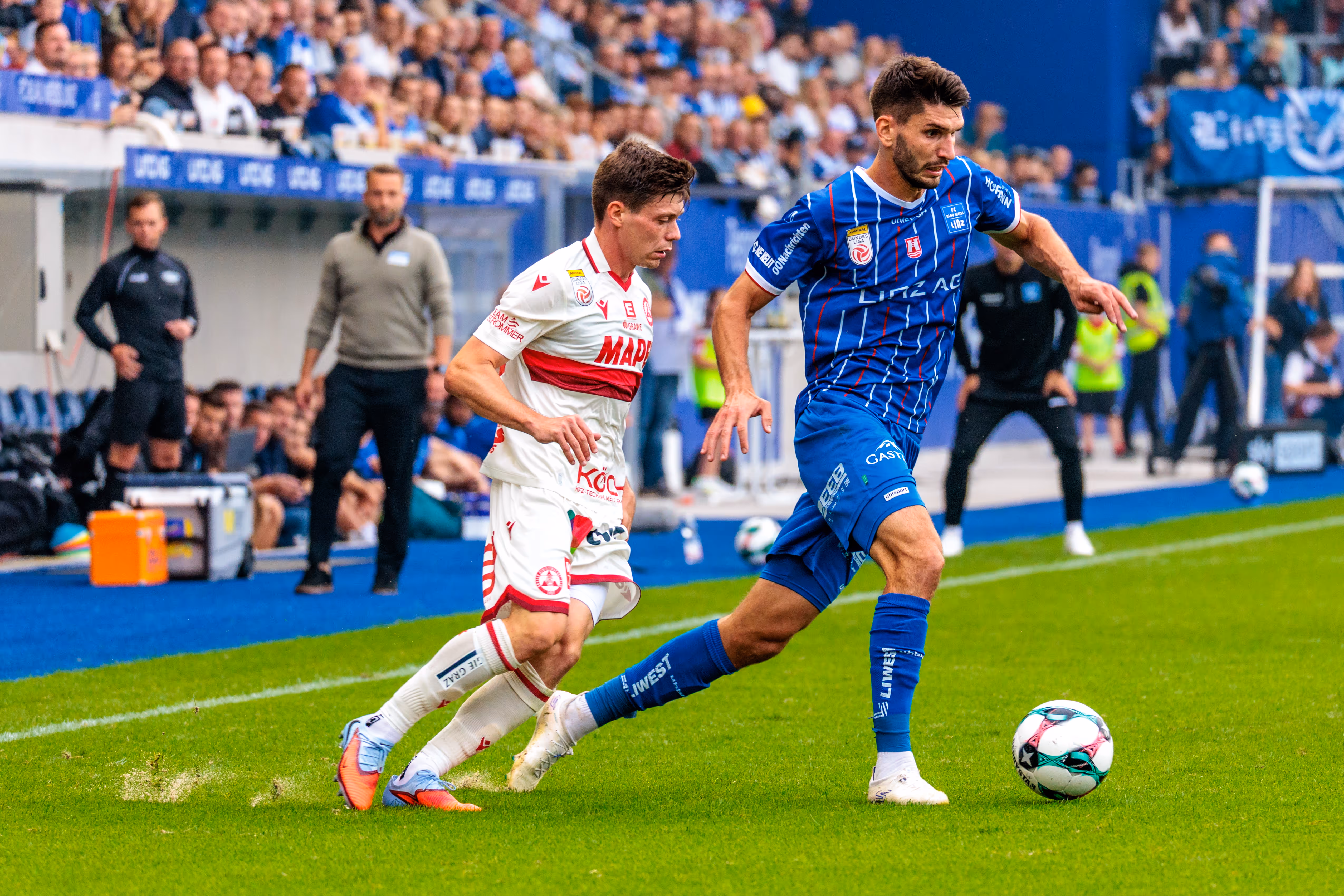 Stürmer Shon Weissman vom FC Blau-Weiß Linz führt den Ball im Dribbling, während ein Gegenspieler des GAK ihn in einem Zweikampf zu stoppen versucht