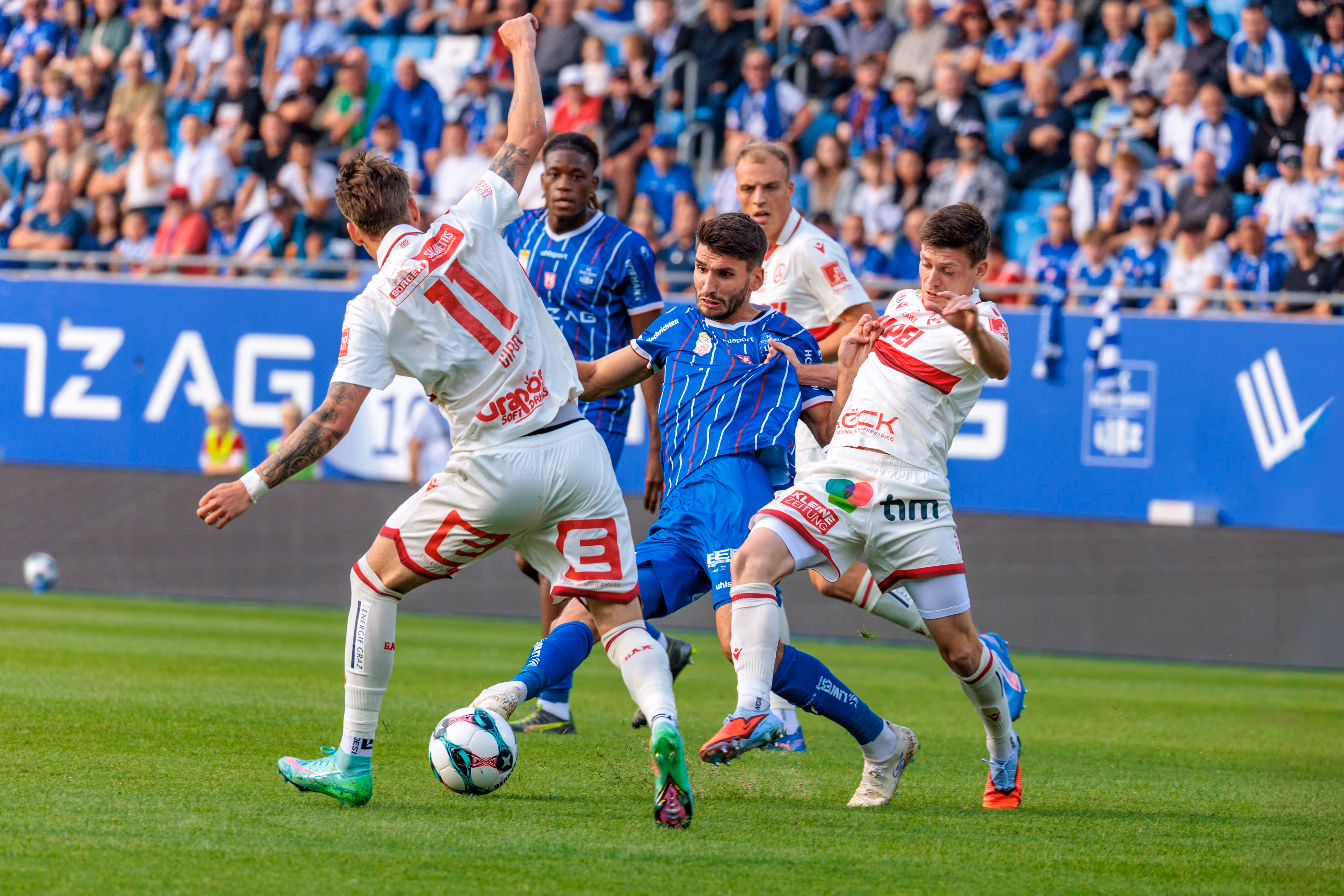 Stürmer Shon Weissman vom FC Blau-Weiß Linz behauptet den Ball in einem intensiven Zweikampf gegen die Verteidiger des GAK während des Bundesligaspiels