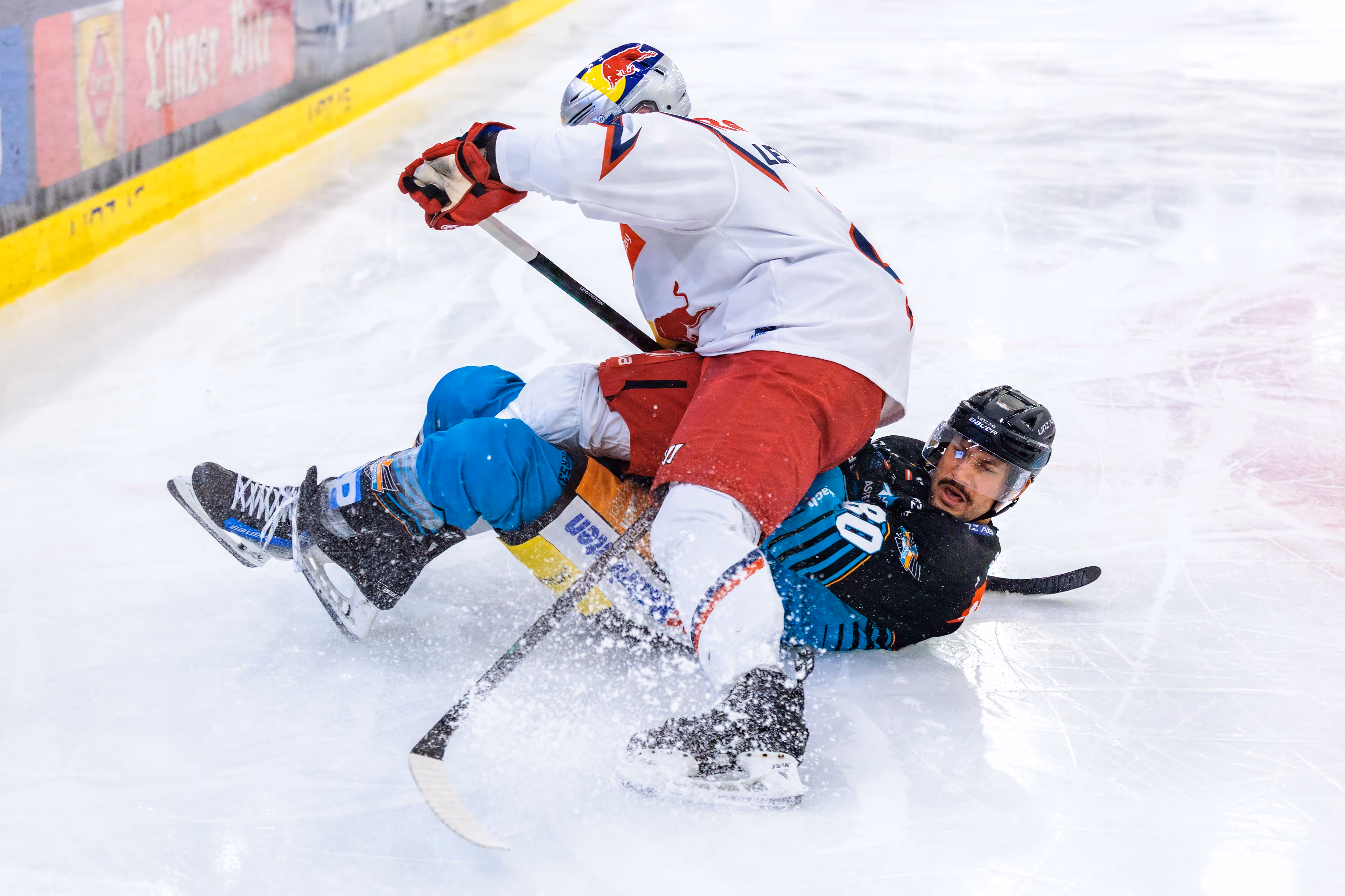 Julian Pusnik von den Steinbach Black Wings Linz wird im intensiven Eishockey-Zweikampf von Tyler Lewington vom EC Red Bull Salzburg zu Boden gerungen