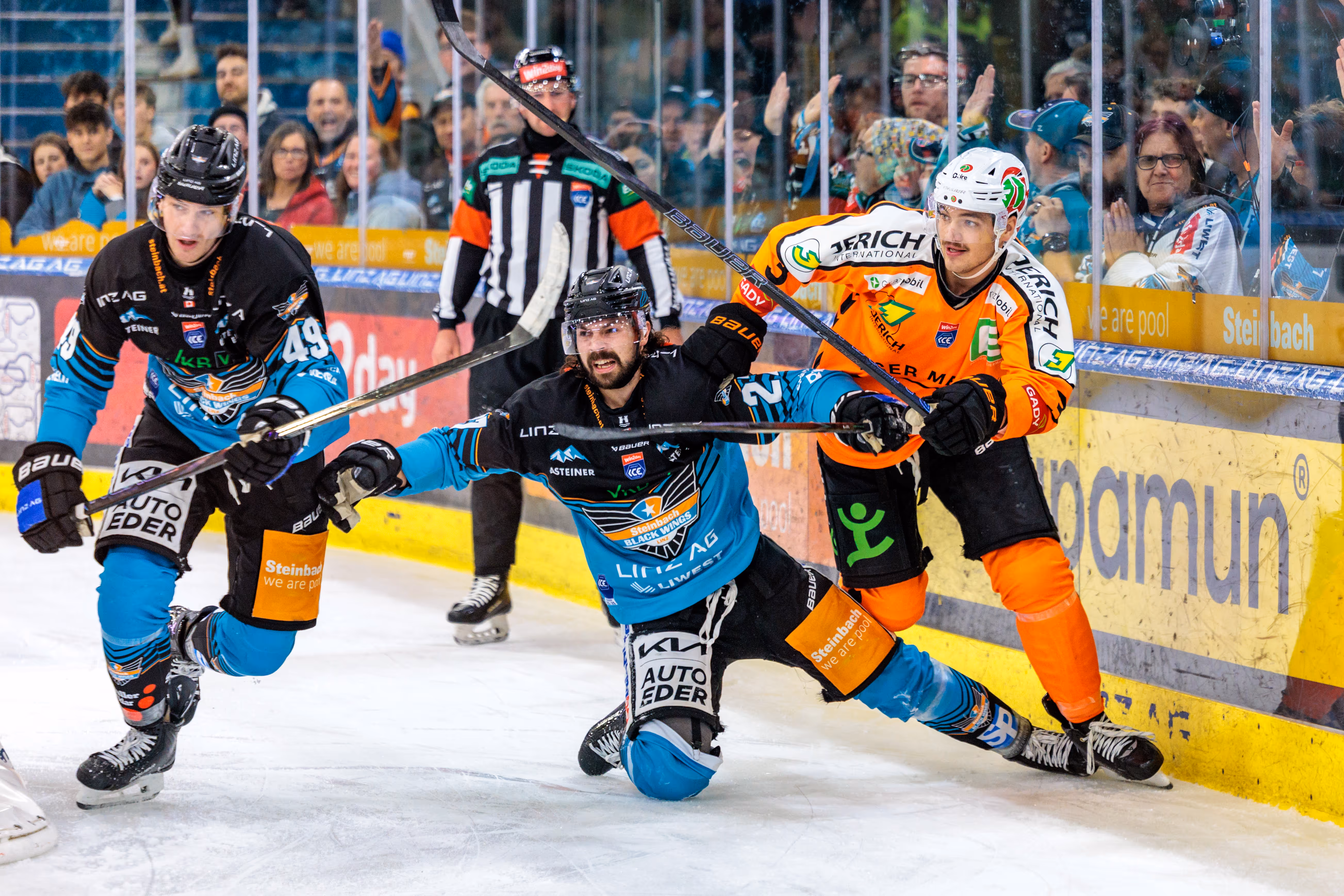 Eishockeyspieler Graham Knott der Black Wings Linz im Zweikampf mit Kevin Roy der Graz99ers nahe der Bande, wobei Knott auf dem Eis gleitet