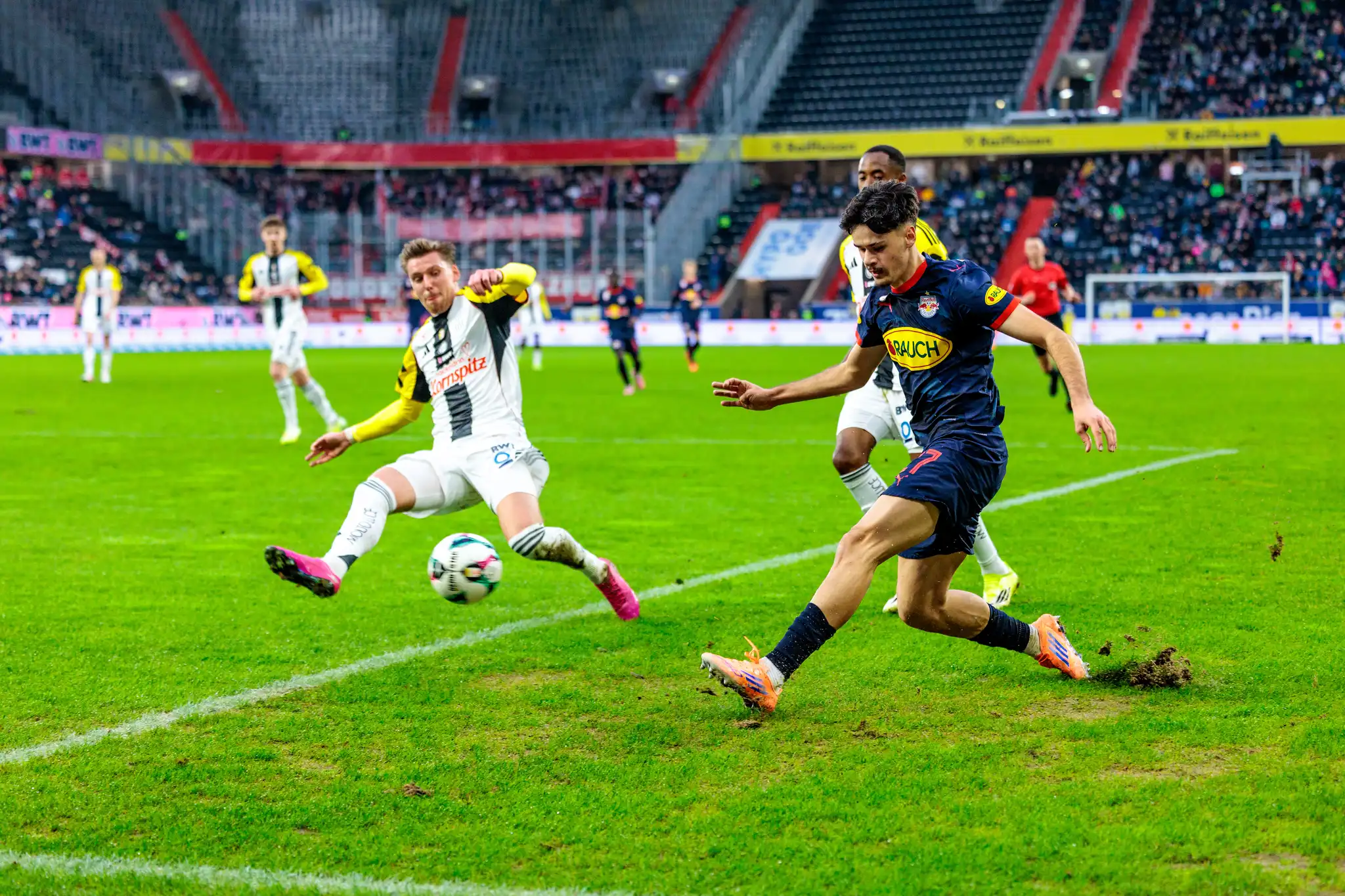 Ein Spieler von Red Bull Salzburg behauptet im intensiven Zweikampf den Ball gegen einen grätschenden Verteidiger des LASK während der Admiral Bundesliga