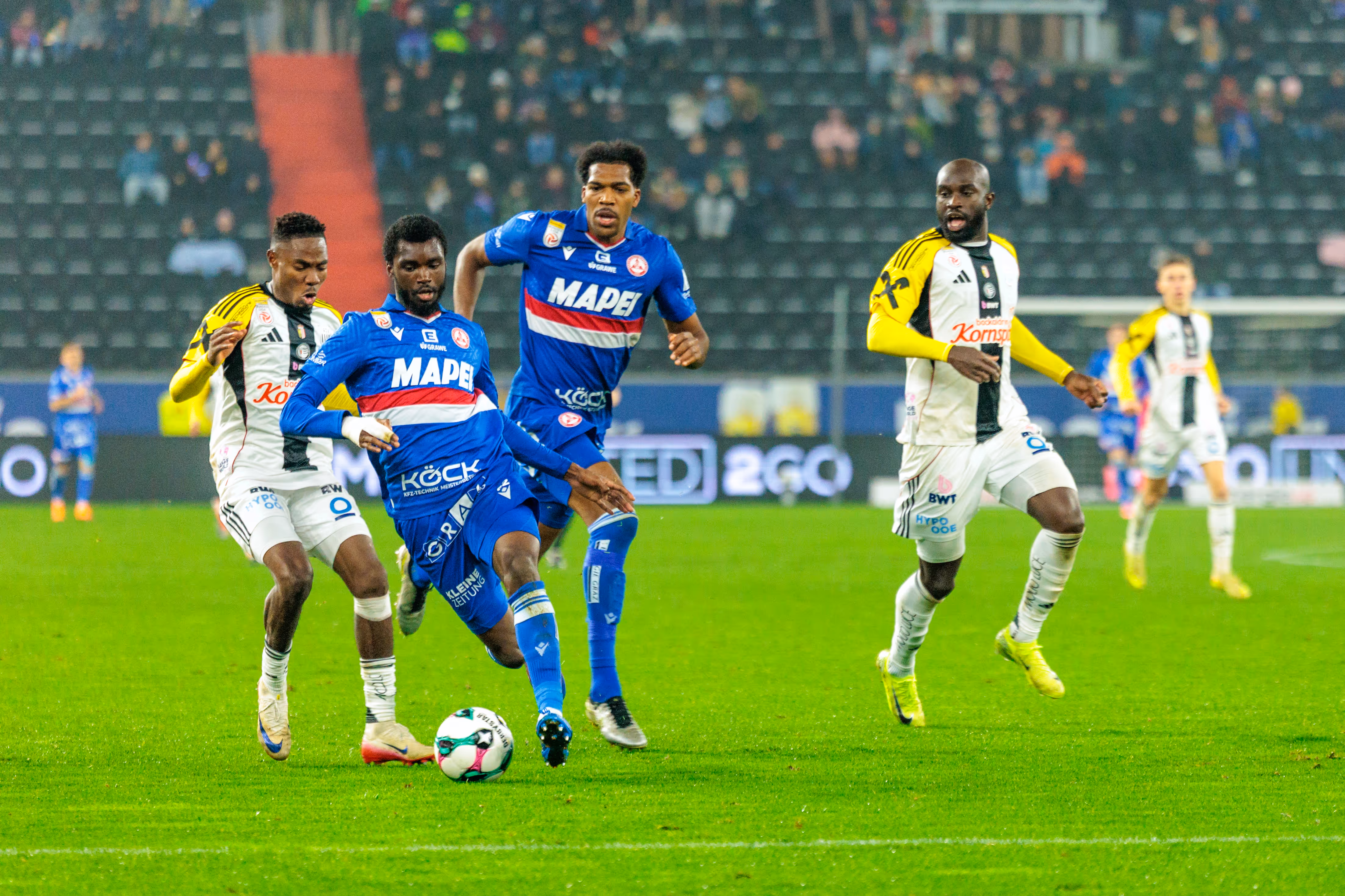 GAK-Spieler Beres Owusu führt den Ball im Mittelfeld und wird im Bundesligaspiel von den LASK-Spielern Moses Usor und George Bello attackiert