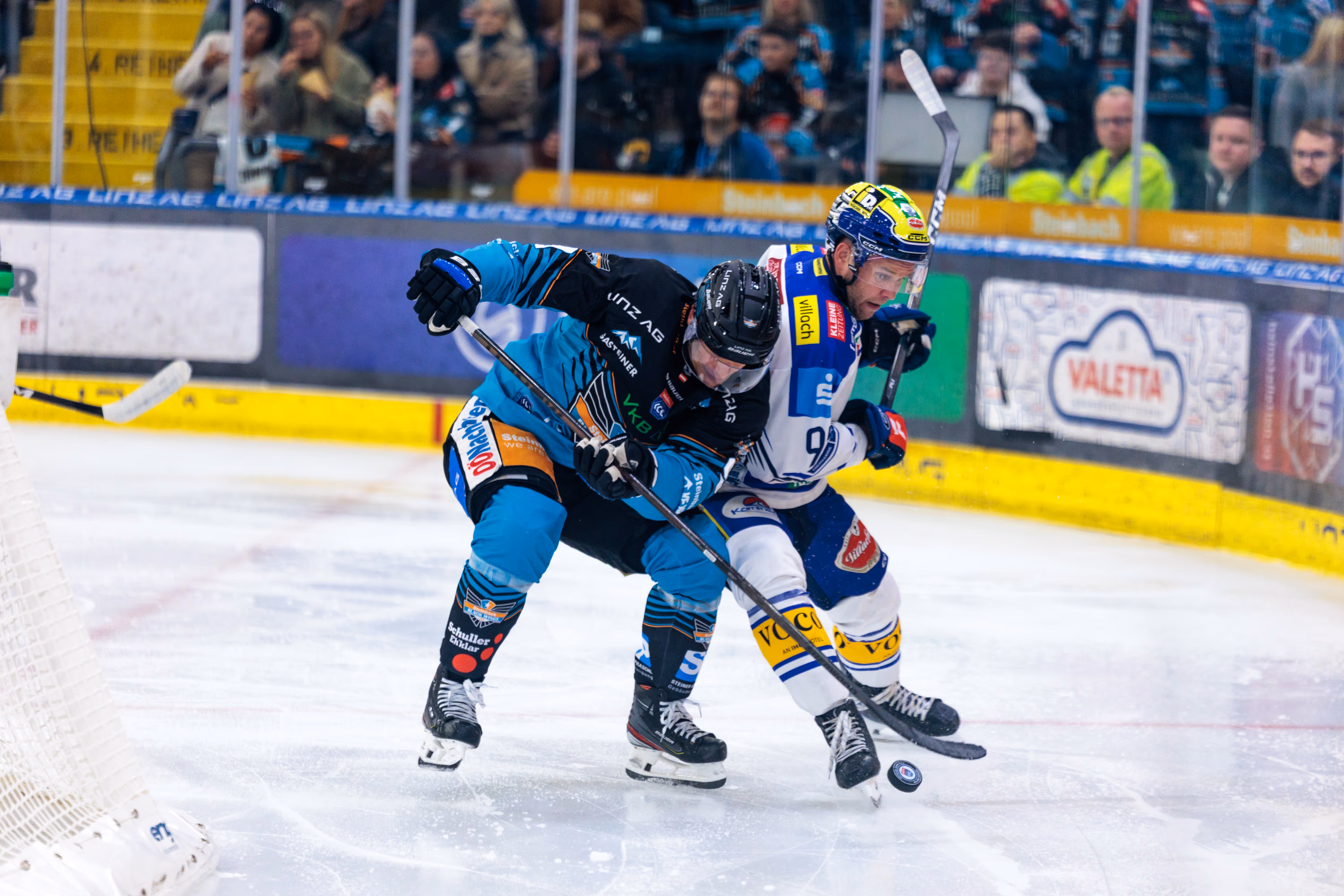 Aljaz Predan von den Black Wings Linz und Mark Katic vom EC VSV kämpfen während eines Eishockeyspiels intensiv um den Puck auf dem Eis