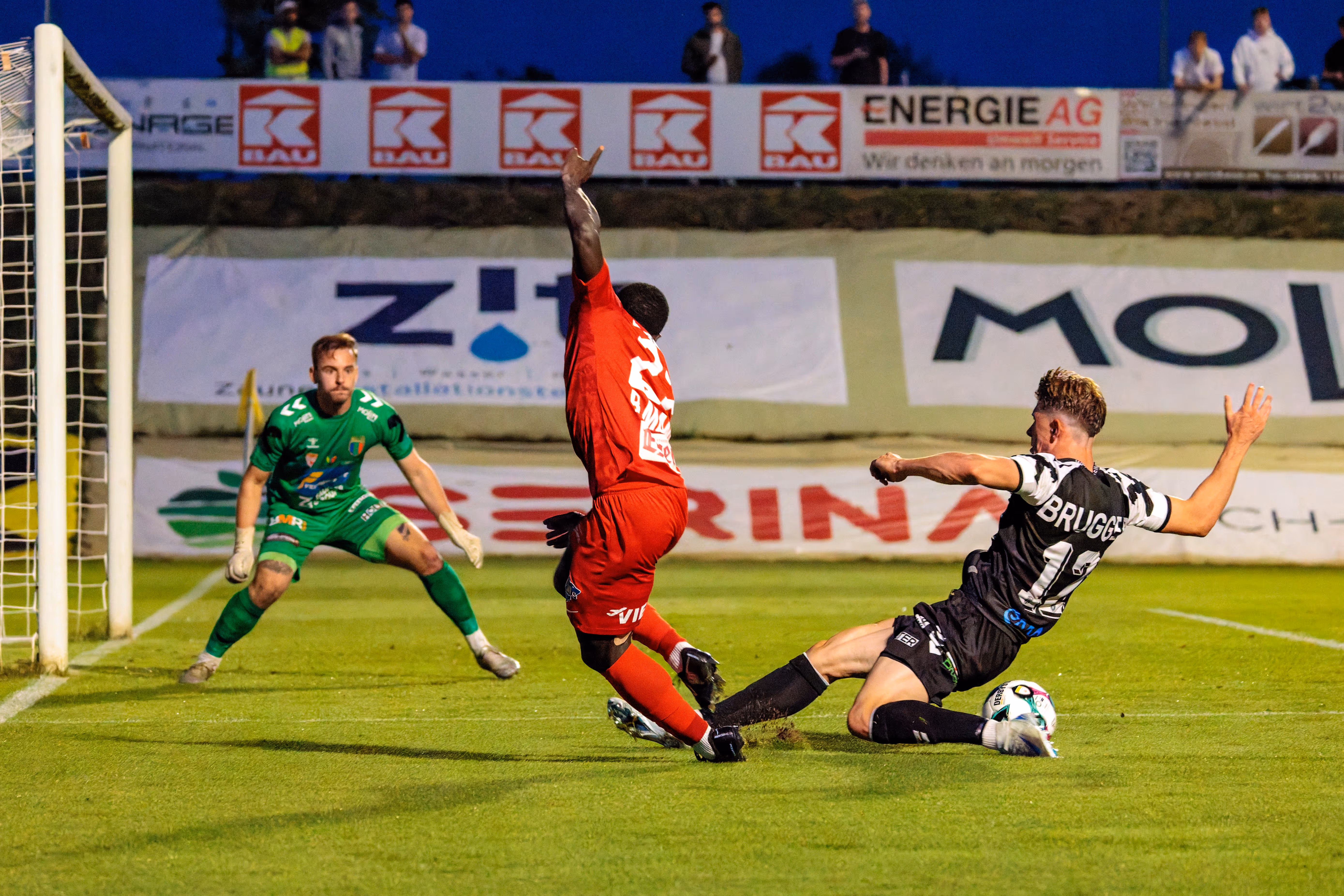 Michael Brugger von SPG HOGO Wels im schwarz-weiß gestreiften Trikot rutscht im ÖFB-Cup im Strafraum in einen Zweikampf um den Ball mit einem Spieler des SKN St. Pölten, während der Welser Torhüter im Hintergrund zuschaut